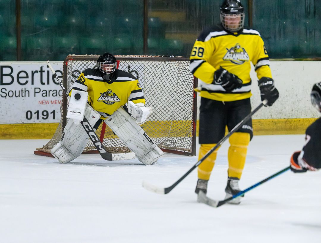 Ice hockey goalkeeper set for the save as defenders protect the goal during a competitive match.