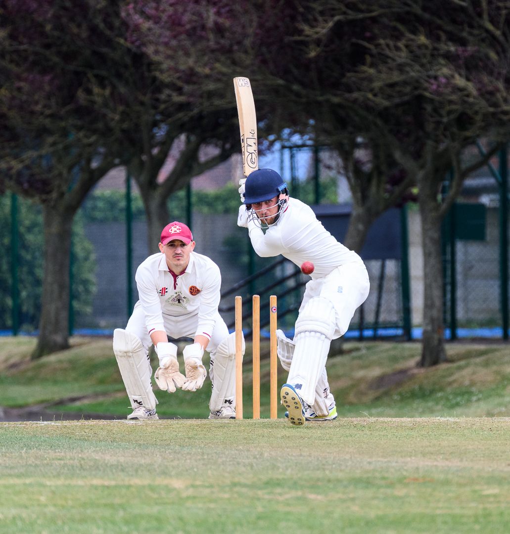 Cricket batsman stretches to defend a delivery during a competitive grassroots cricket match.