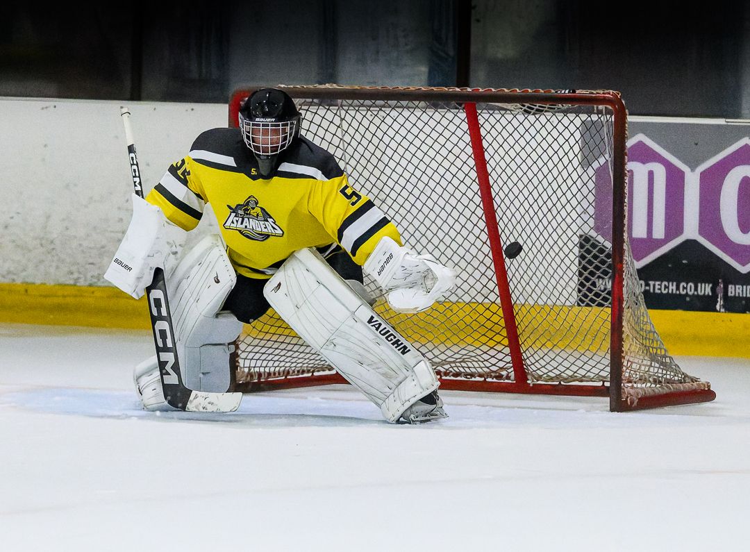 Ice hockey goalkeeper stands ready in front of the net during a competitive ice hockey match.