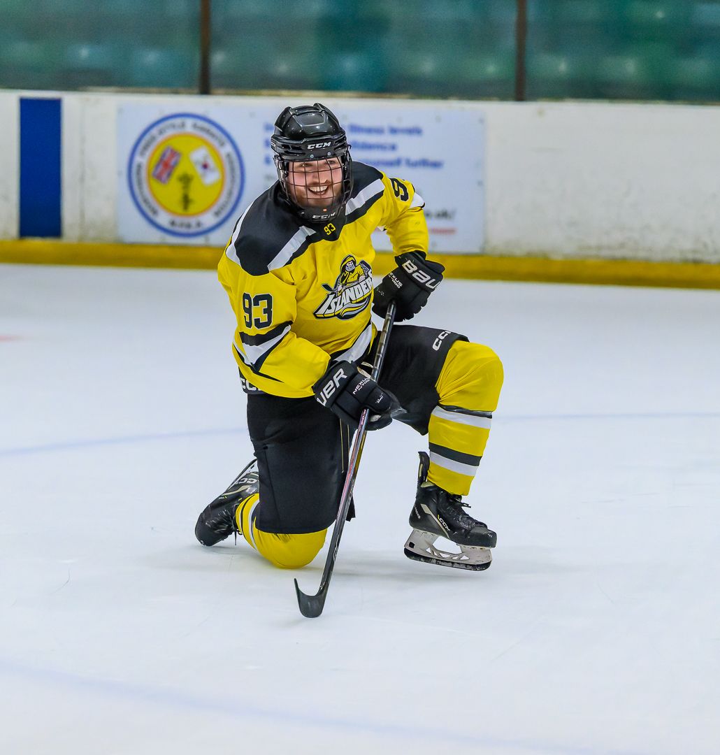 Ice hockey player celebrates on one knee after scoring during a competitive ice hockey match.