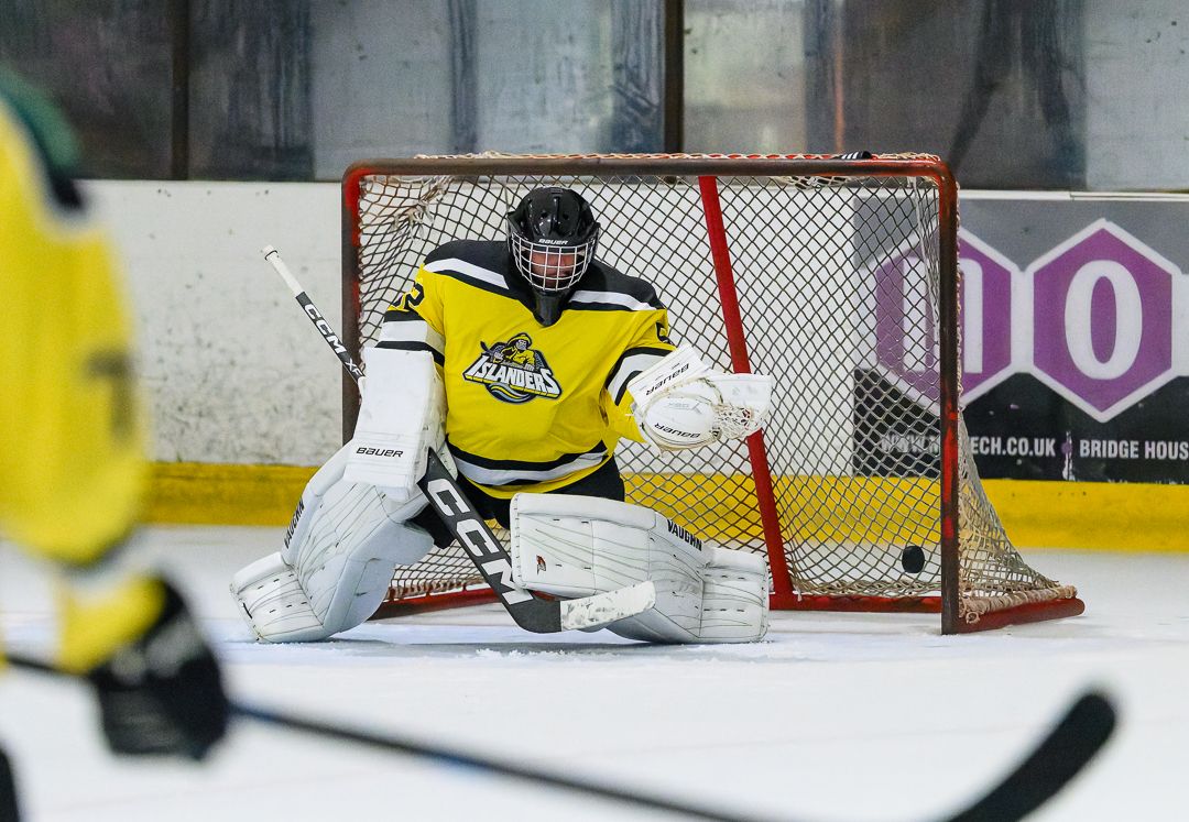 Ice hockey goalkeeper stands ready in front of the net during a competitive ice hockey match.