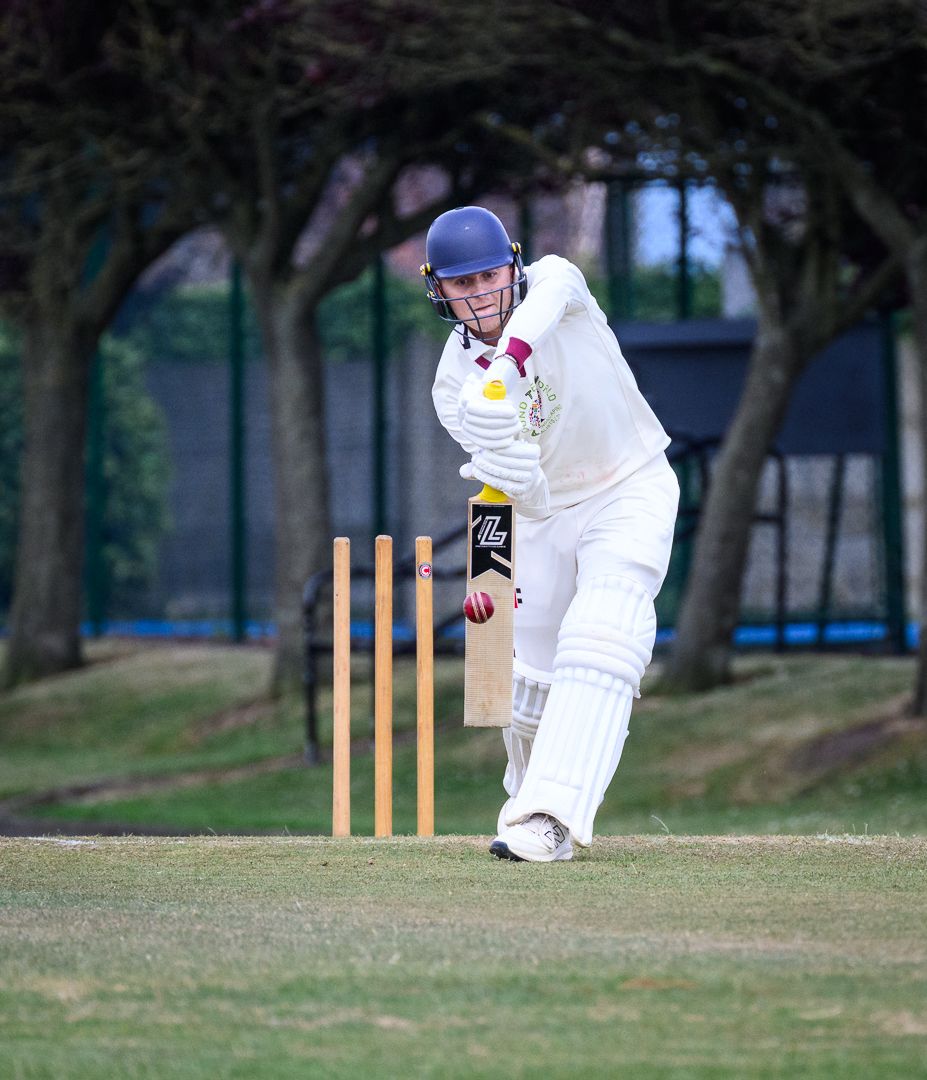 Cricket batsman stretches to defend a delivery during a competitive grassroots cricket match.
