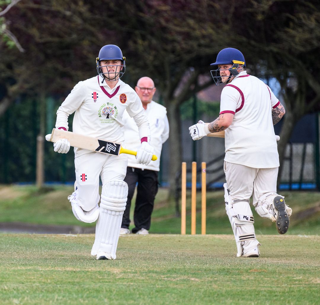 Cricket batsmen sprint between the wickets during a competitive grassroots cricket match.