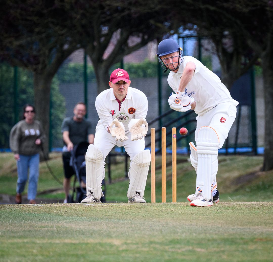 Cricket batsman stretches to defend a delivery during a competitive grassroots cricket match.