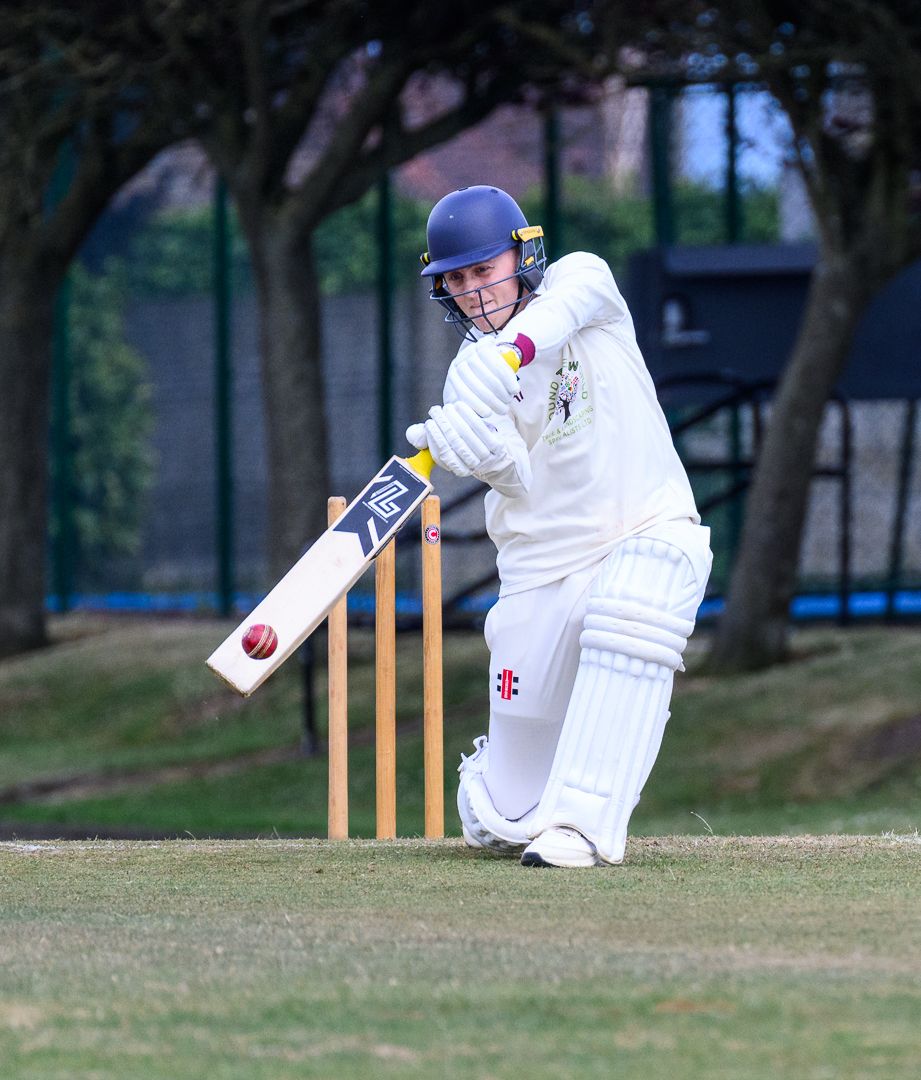 Cricket batsman stretches to defend a delivery during a competitive grassroots cricket match.