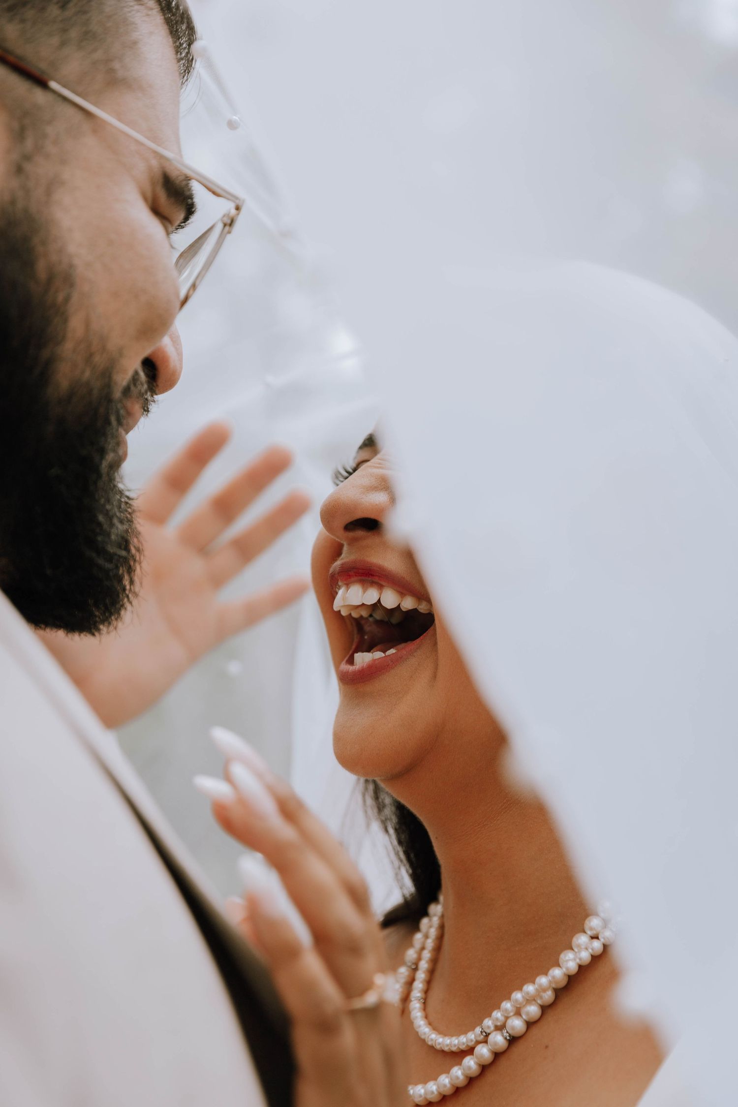 Bride and Groom laugh while looking at each other both under the Bride’s veil