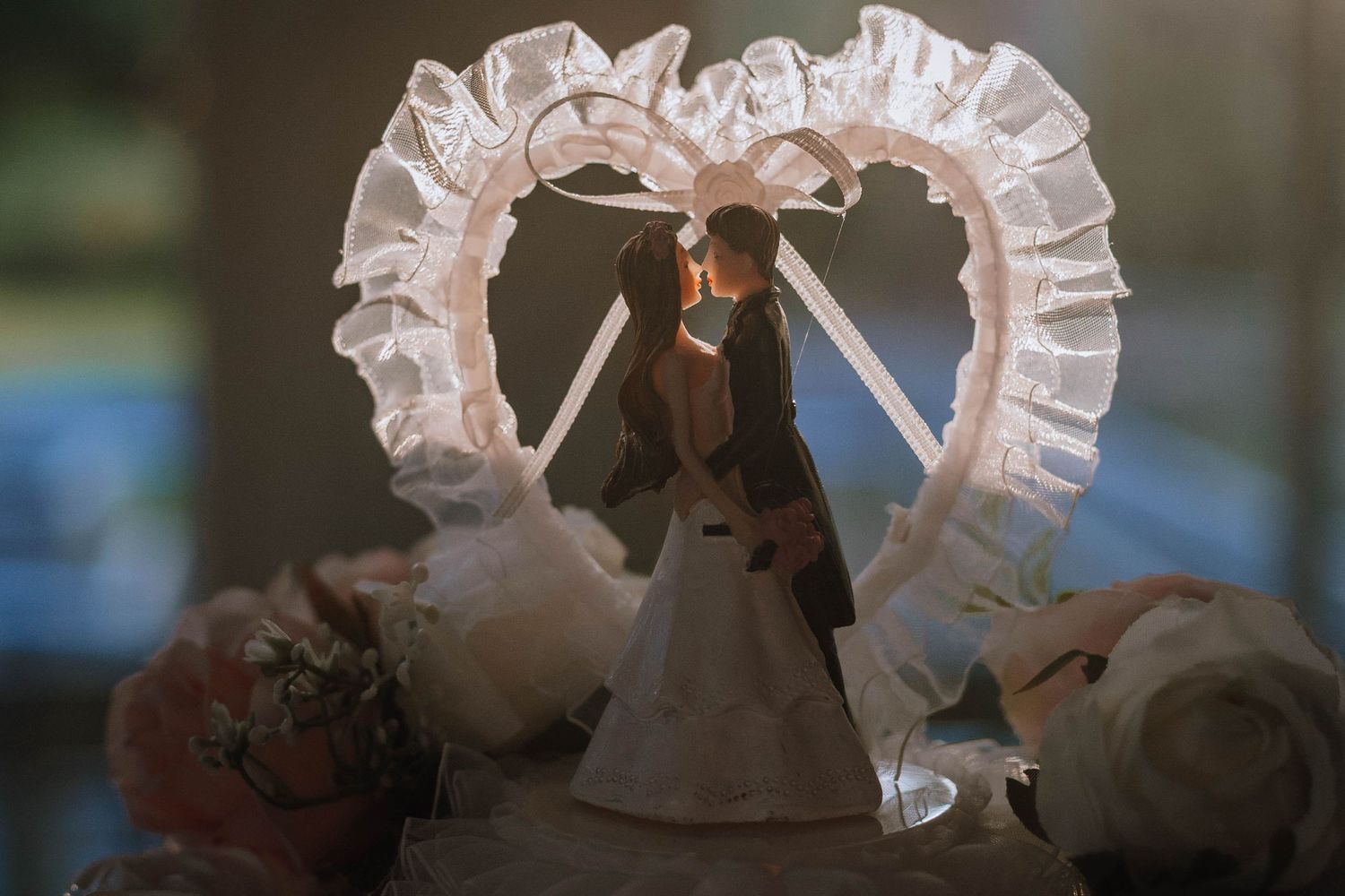 Bride and groom cake topper with mesh ruffled heart topper shining from the sunlight behind it.