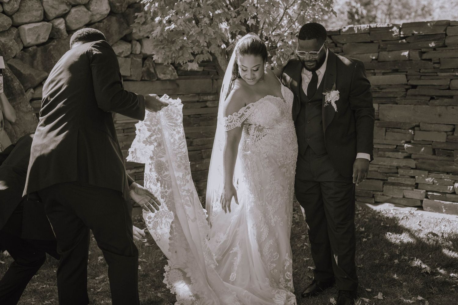 Groomsmen help bride with her dress while it romantically catches the sunlight