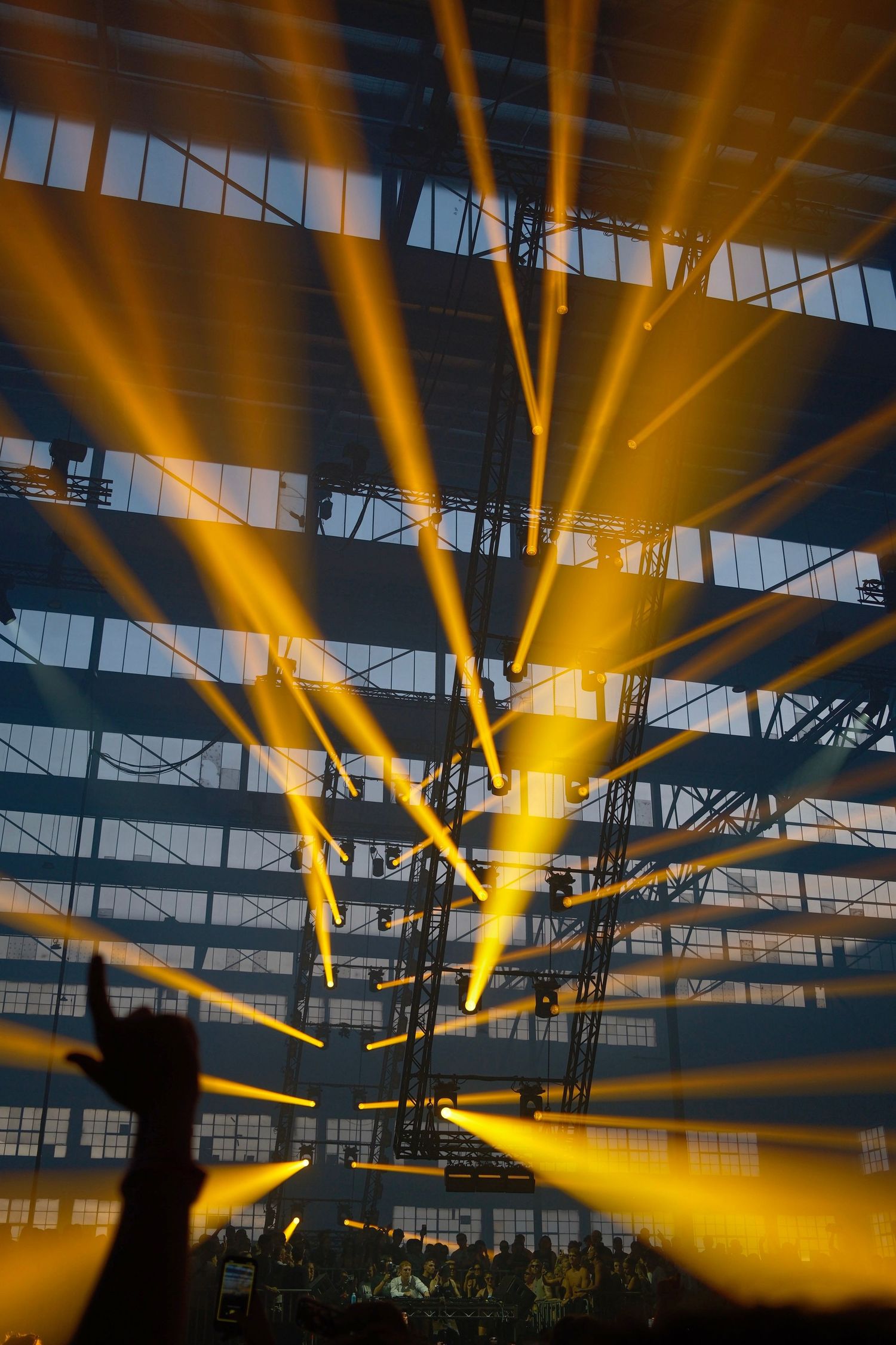 Spectacular golden light beams radiating across an industrial warehouse concert venue ceiling.