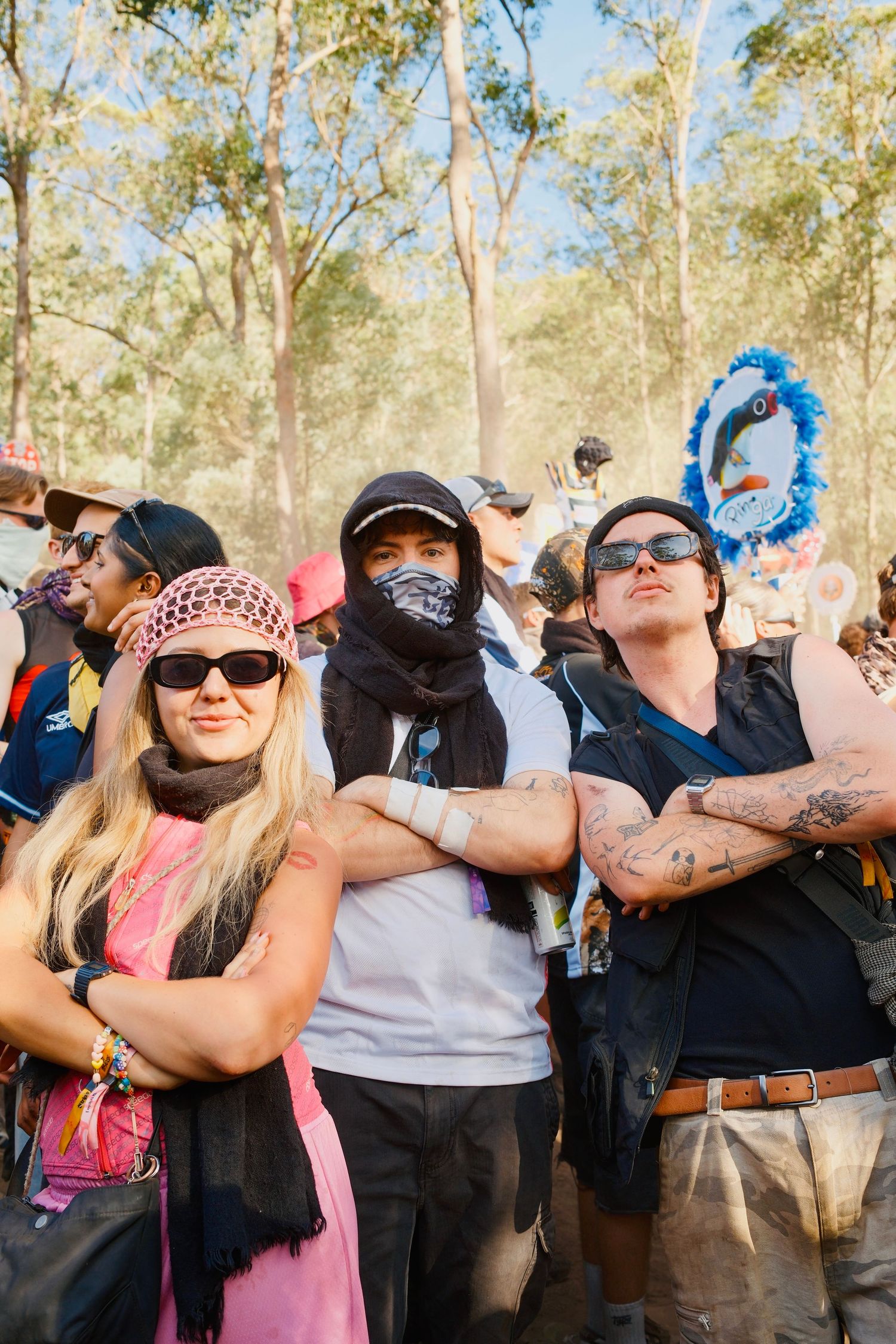 Three tattooed festival attendees posing with arms crossed at an outdoor music festival.