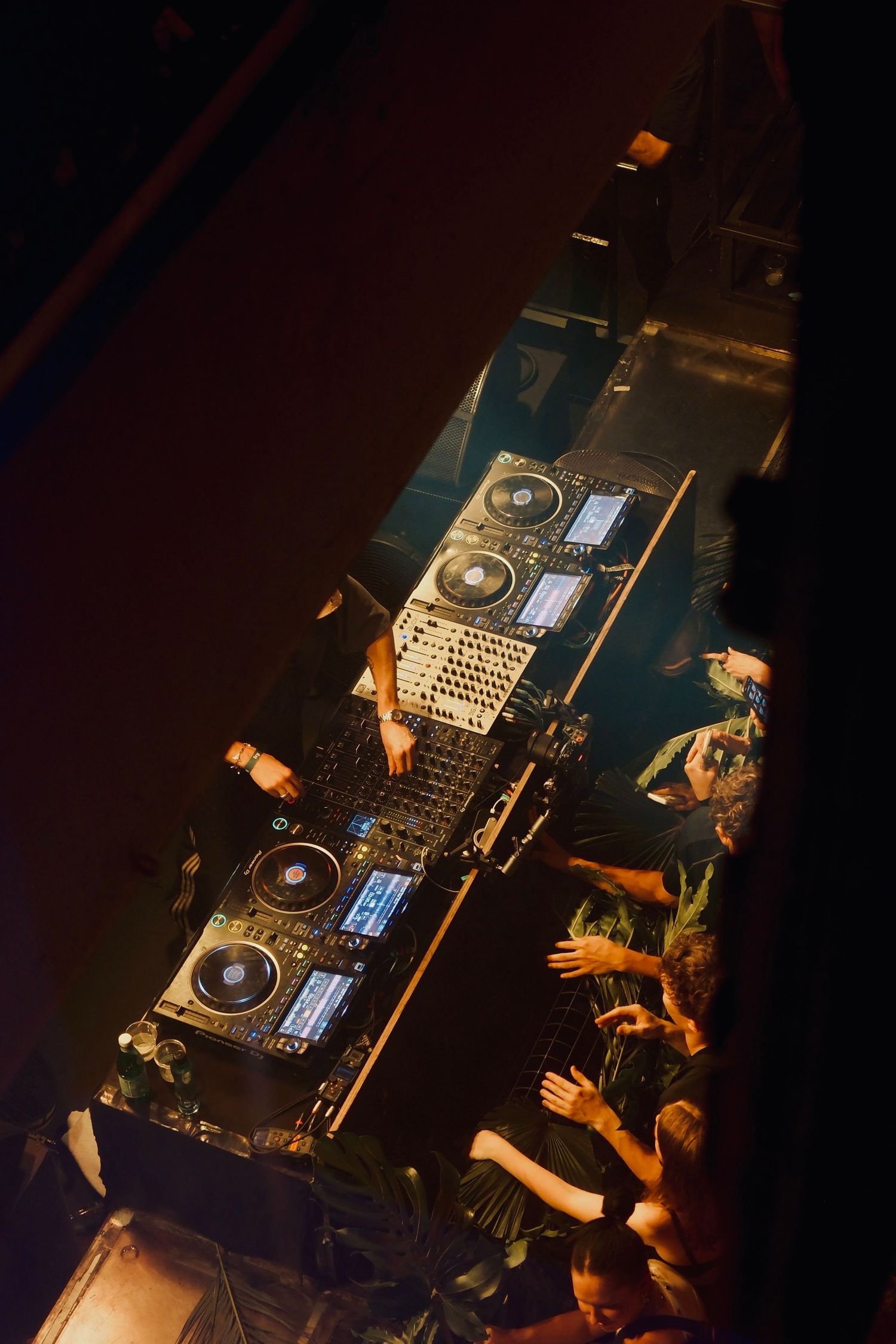 Overhead aerial view of DJ equipment and turntables with crowd reaching toward the DJ booth.