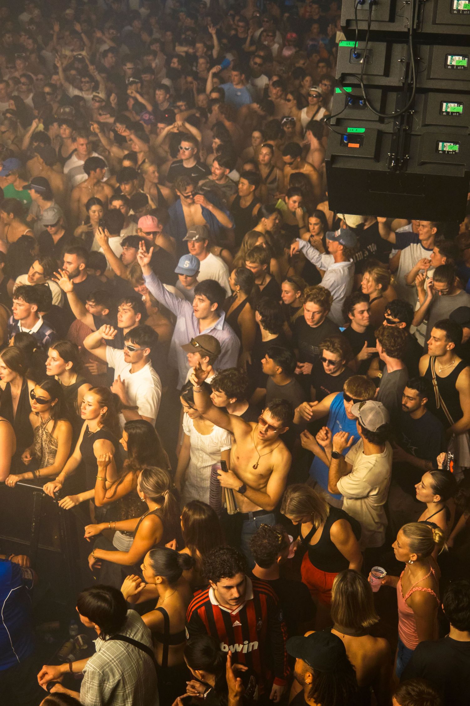 Large crowd of young people packed together at an indoor concert or nightclub event with dramatic lighting.