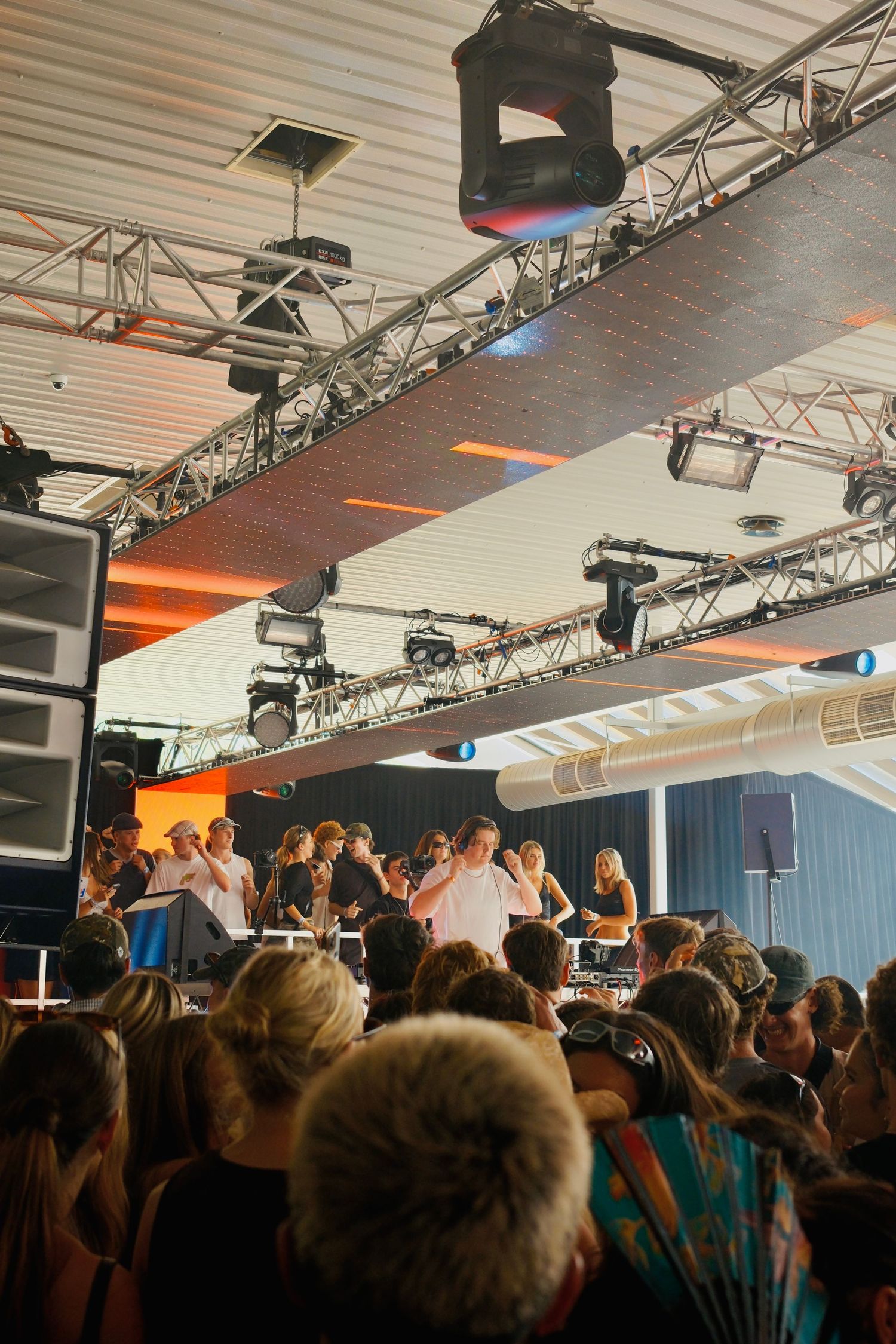 Crowd enjoying a live performance under stage lighting rigs at an outdoor covered music festival event.