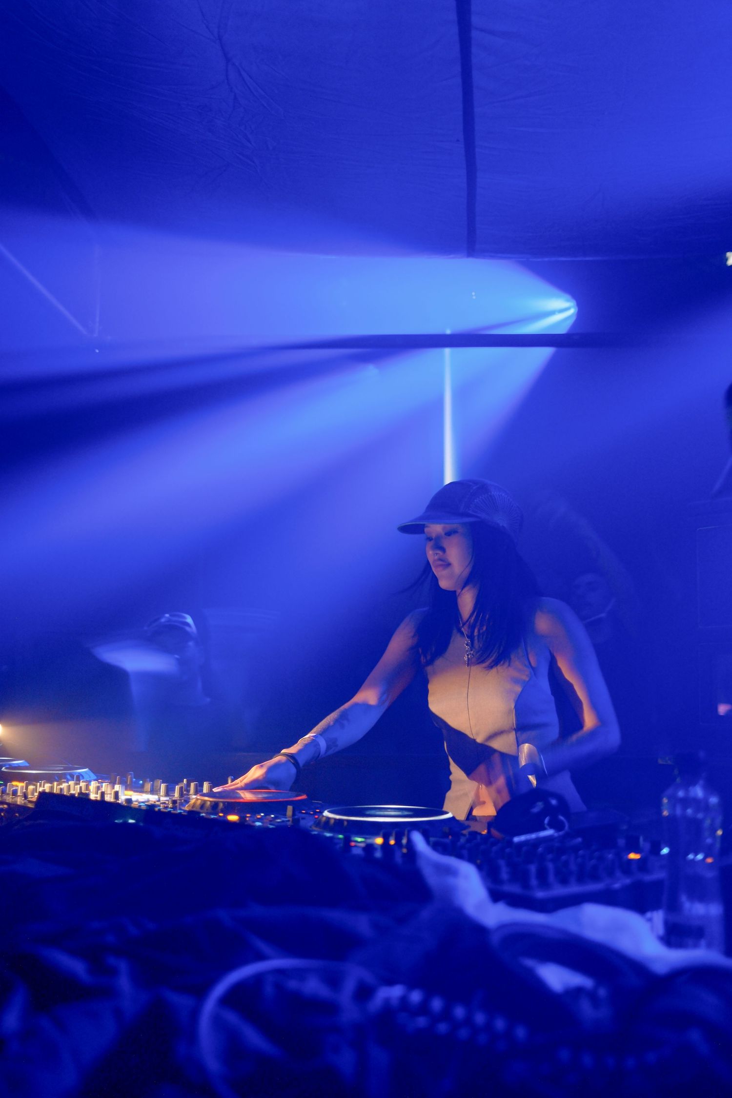 Female DJ performing at a nightclub under blue stage lights, mixing tracks on professional turntables.