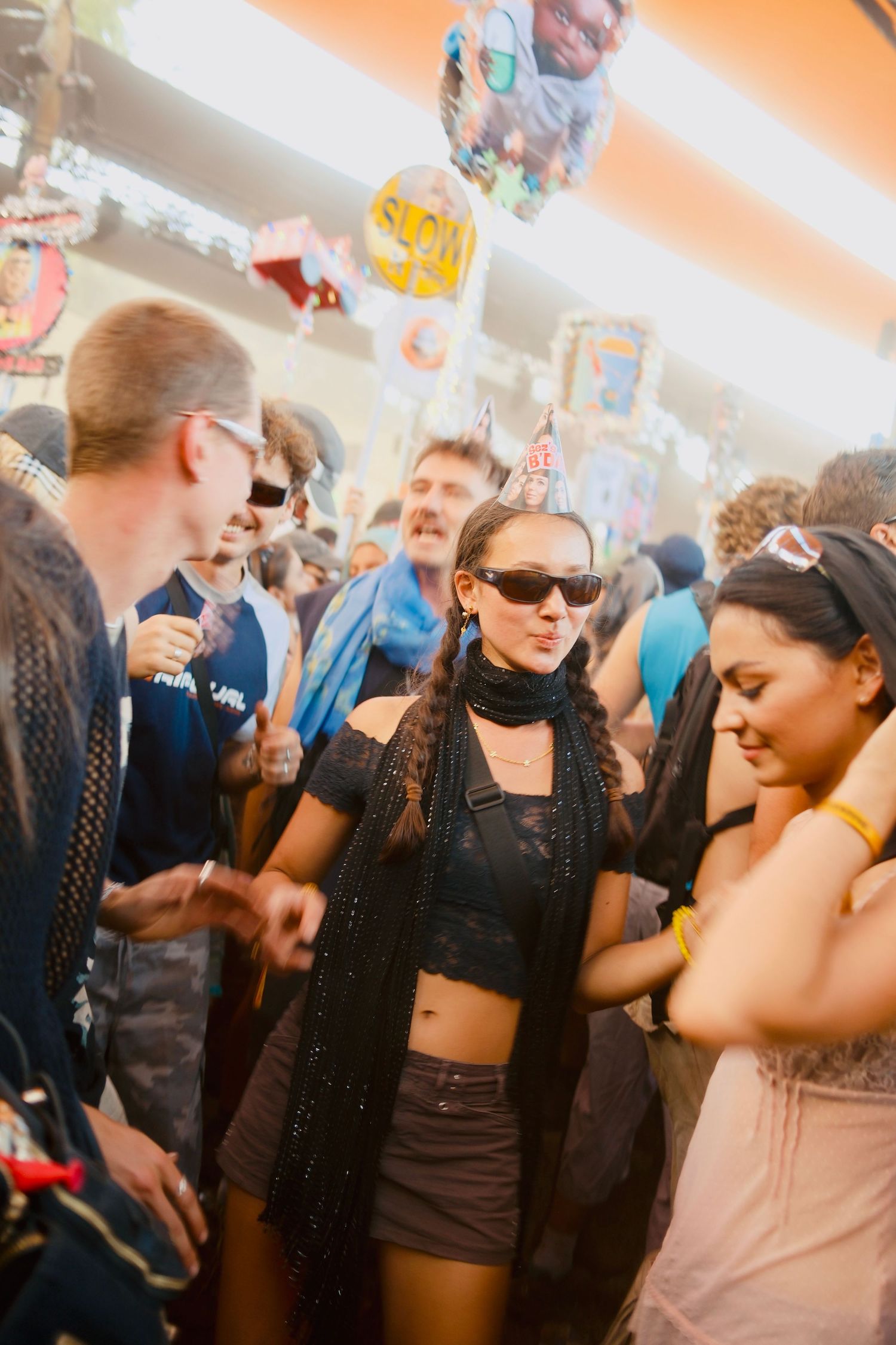 Woman in black outfit and party hat dancing in a vibrant festival crowd.