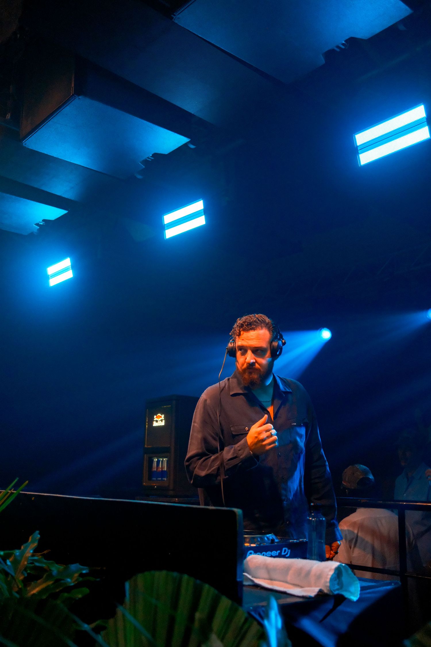 DJ performing under blue stage lights with headphones around neck at a nightclub event.