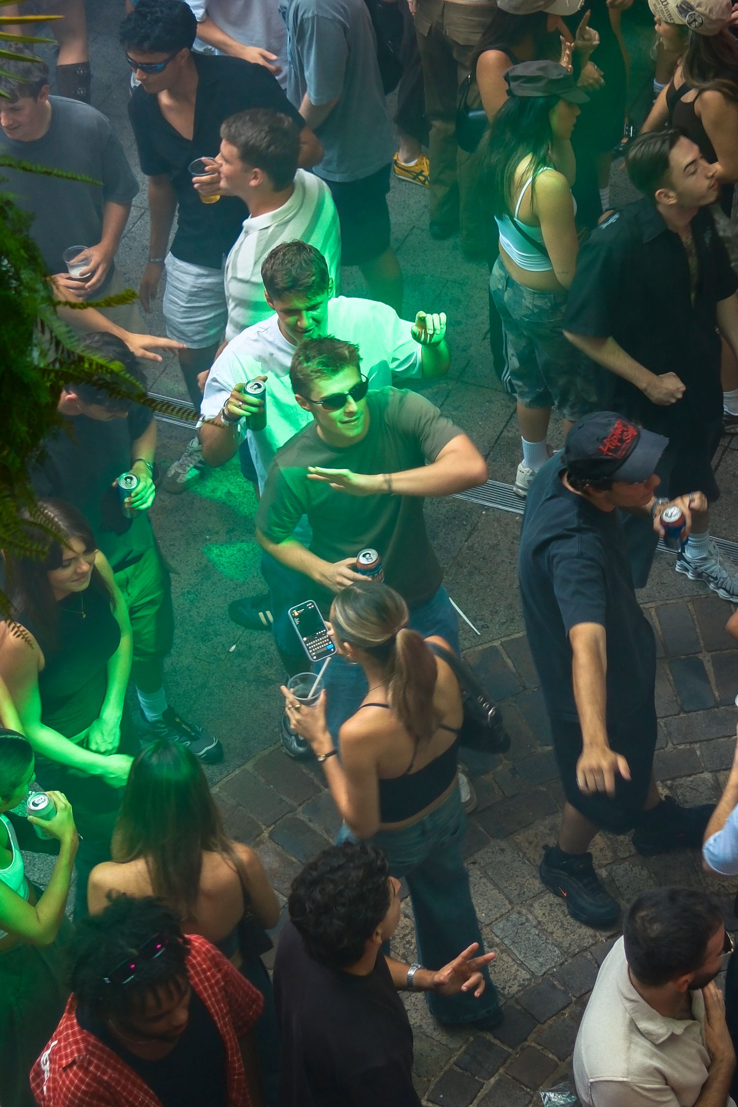 Crowd of young people dancing under green lights at a vibrant nightclub party.