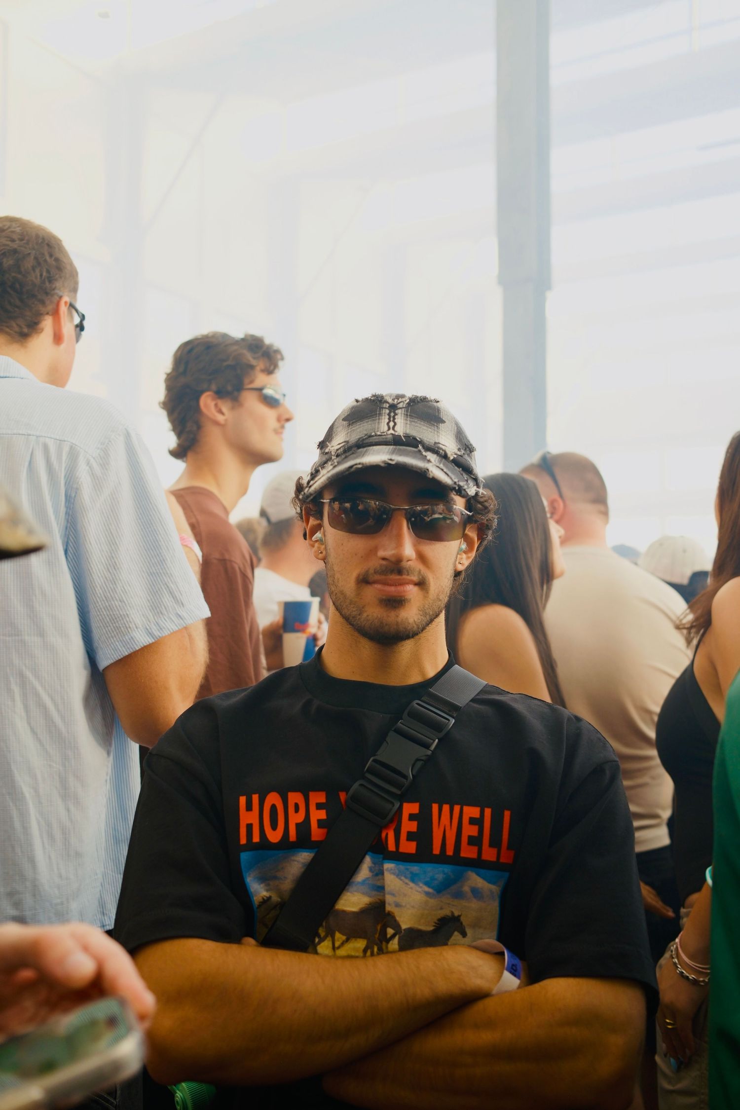Young man in a Hope We Well shirt and cap poses at an outdoor music festival.