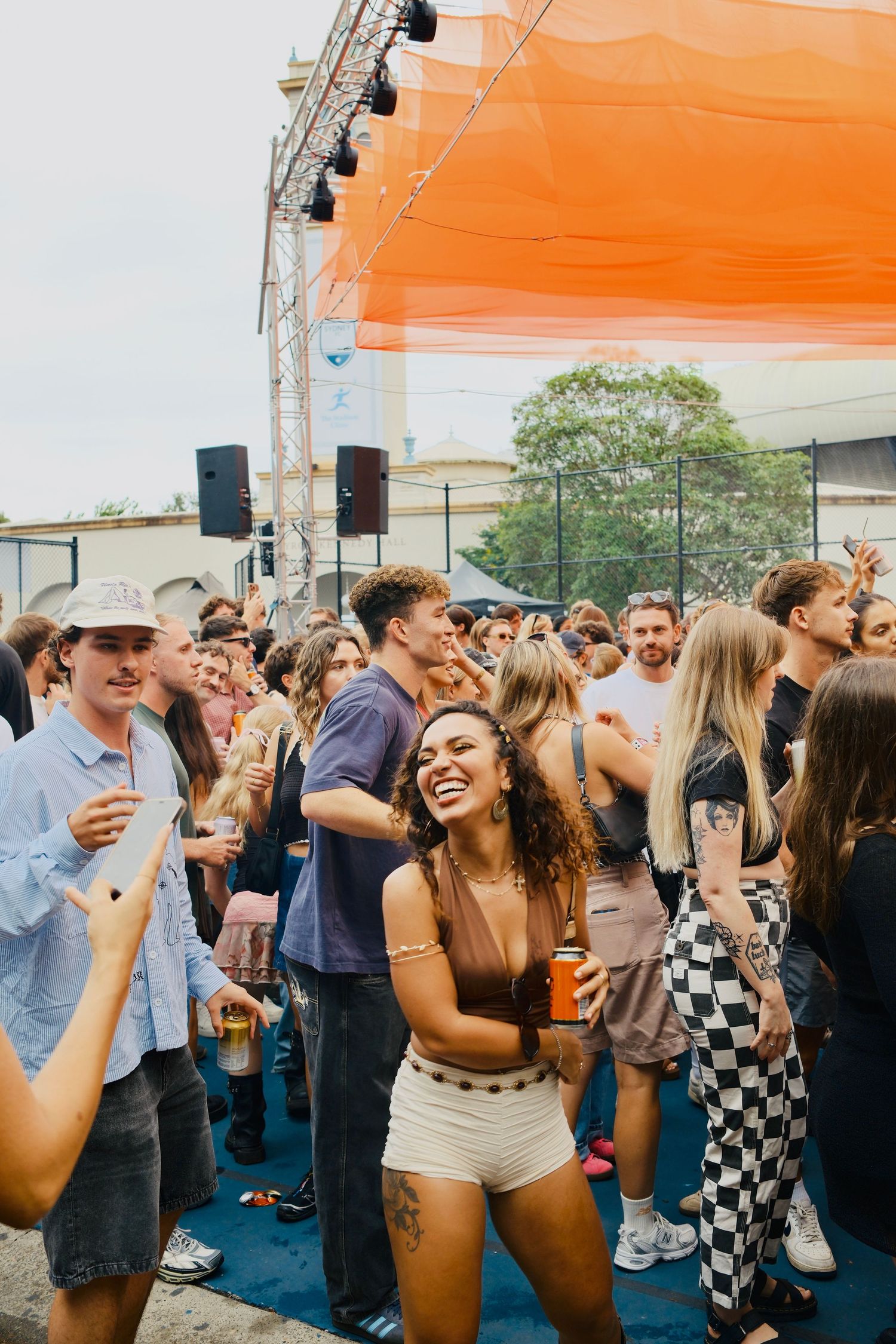 Happy young woman with curly hair dancing and smiling in a crowd at an outdoor music festival.