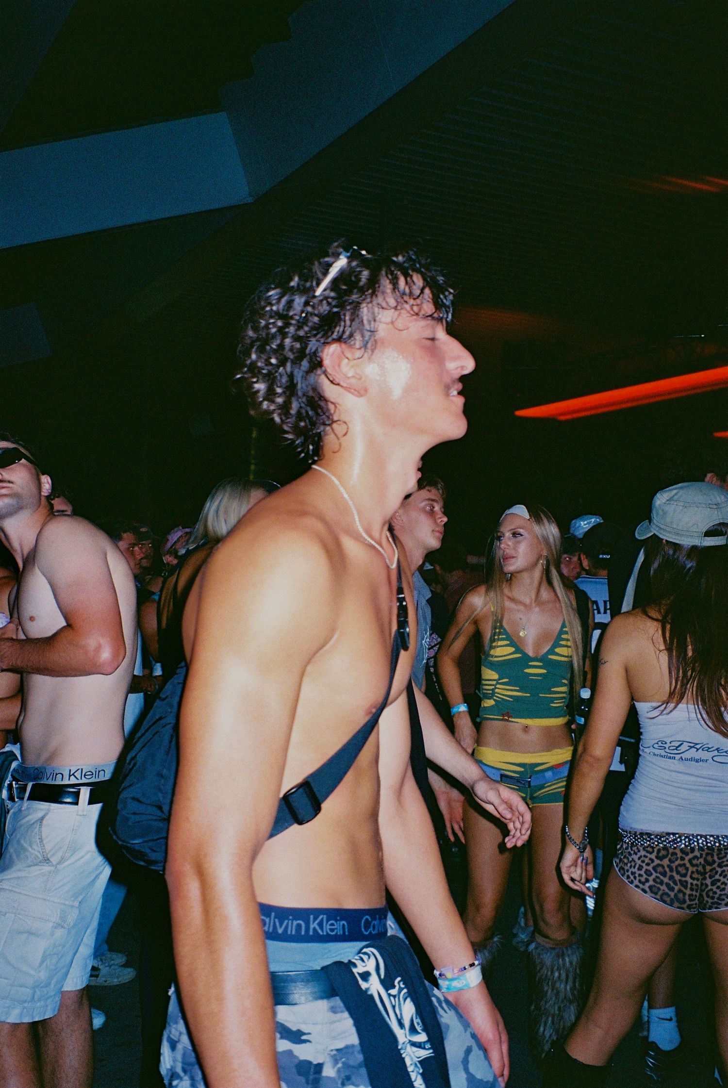 Shirtless young man dancing energetically at crowded indoor music festival.