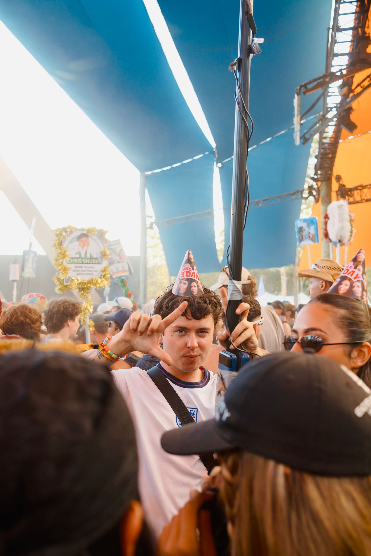 Young man wearing a party hat making a peace sign in a crowded outdoor music festival.