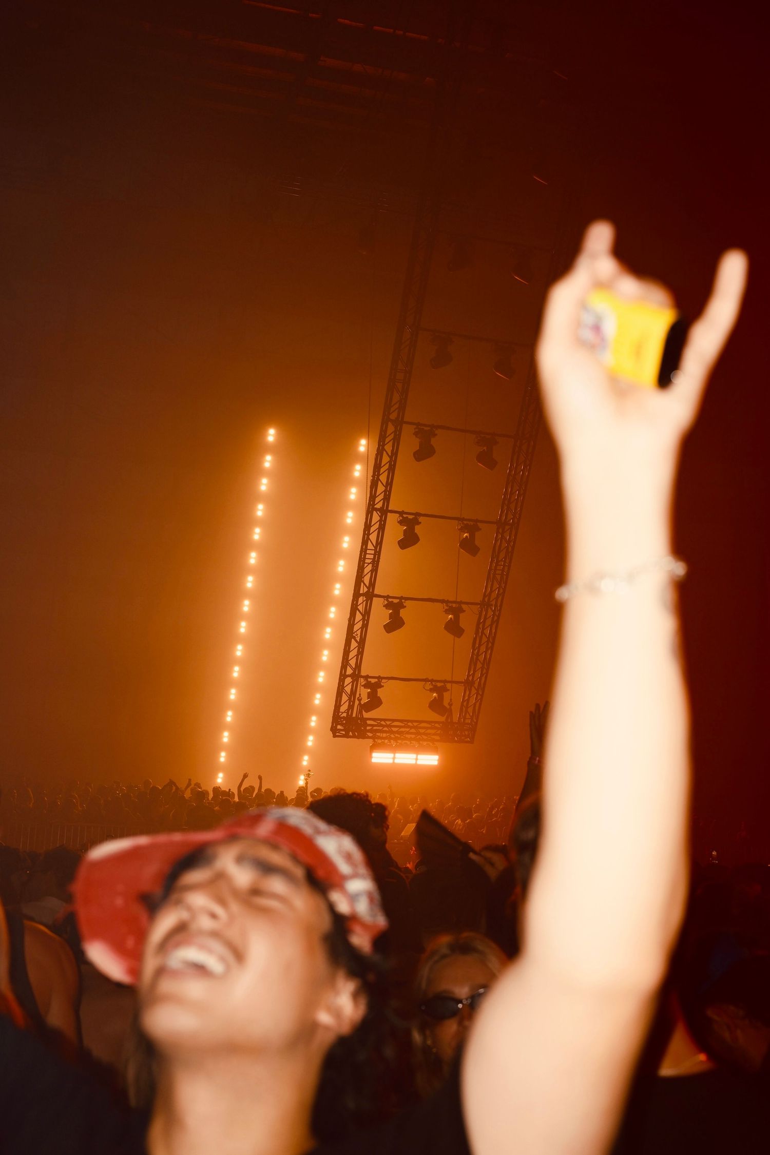 Concert-goer raising a drink under warm orange stage lights at an indoor music event.