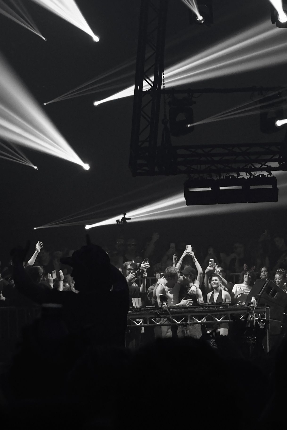 Black and white photo of a DJ set with dramatic stage lighting beams at a concert.