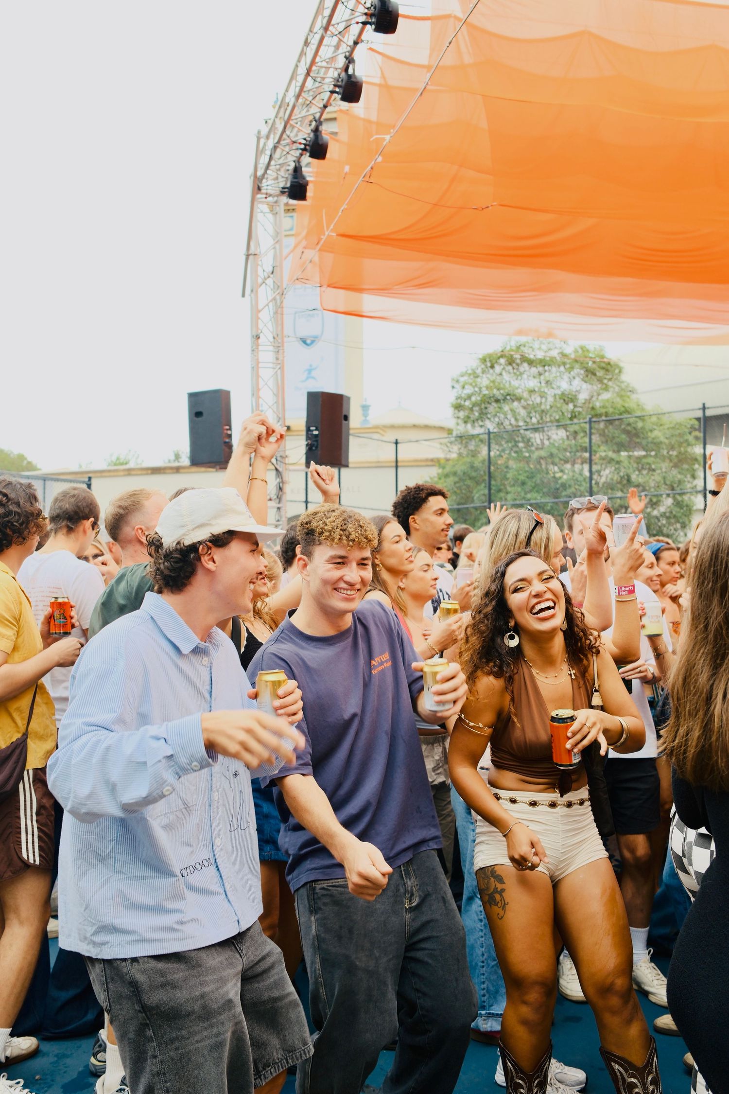 Group of friends dancing and laughing together in front of an orange-canopied outdoor festival stage.