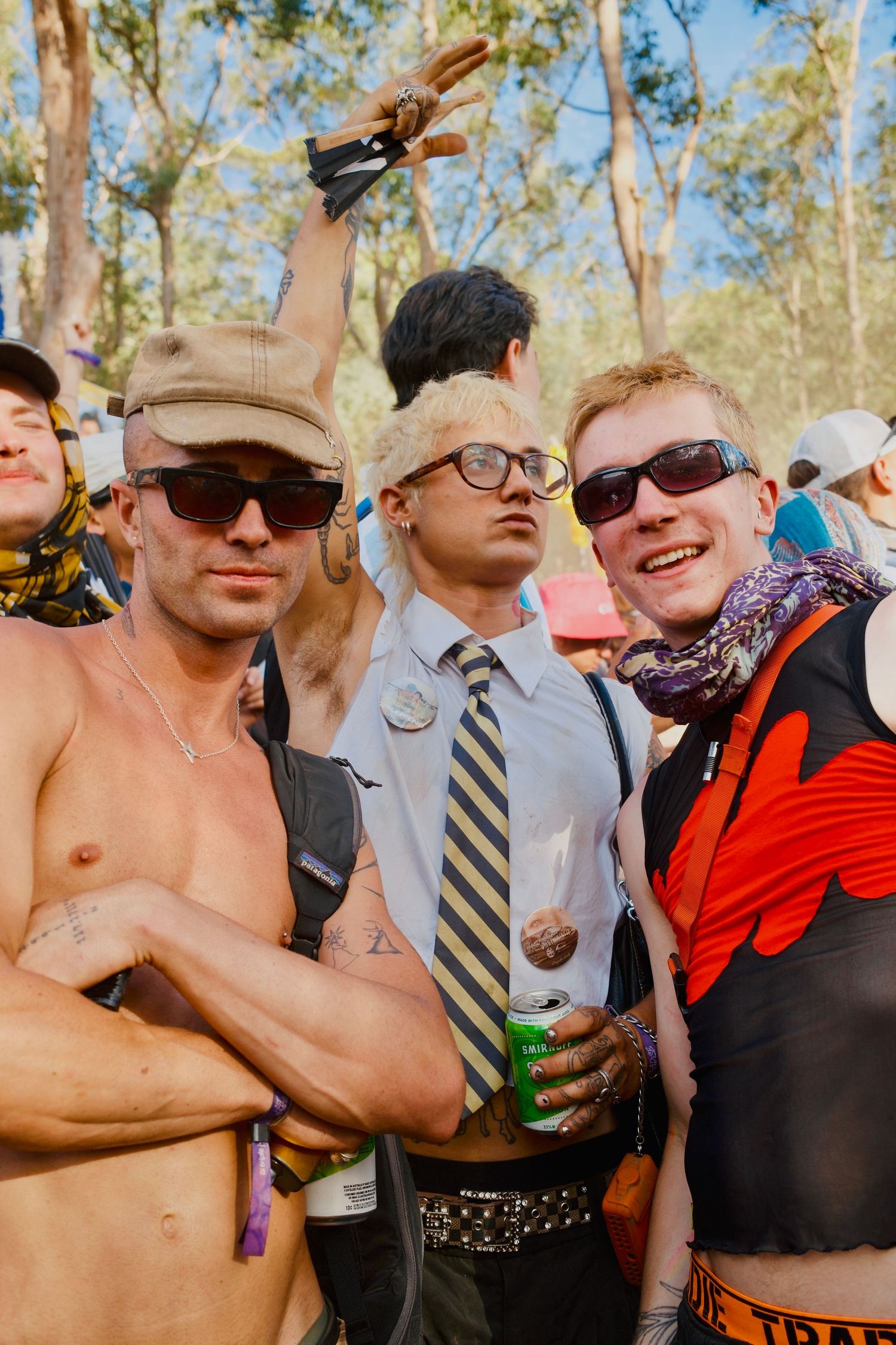 Three festival-goers posing in costumes and sunglasses at an outdoor music festival.