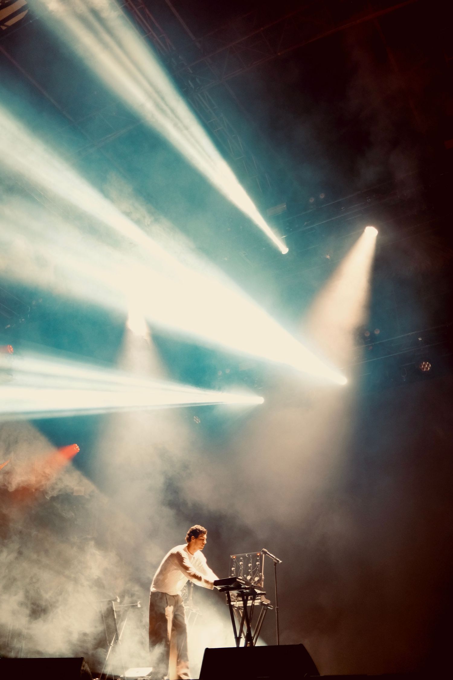 DJ performing on stage surrounded by dramatic light beams and smoke at a live music concert event.
