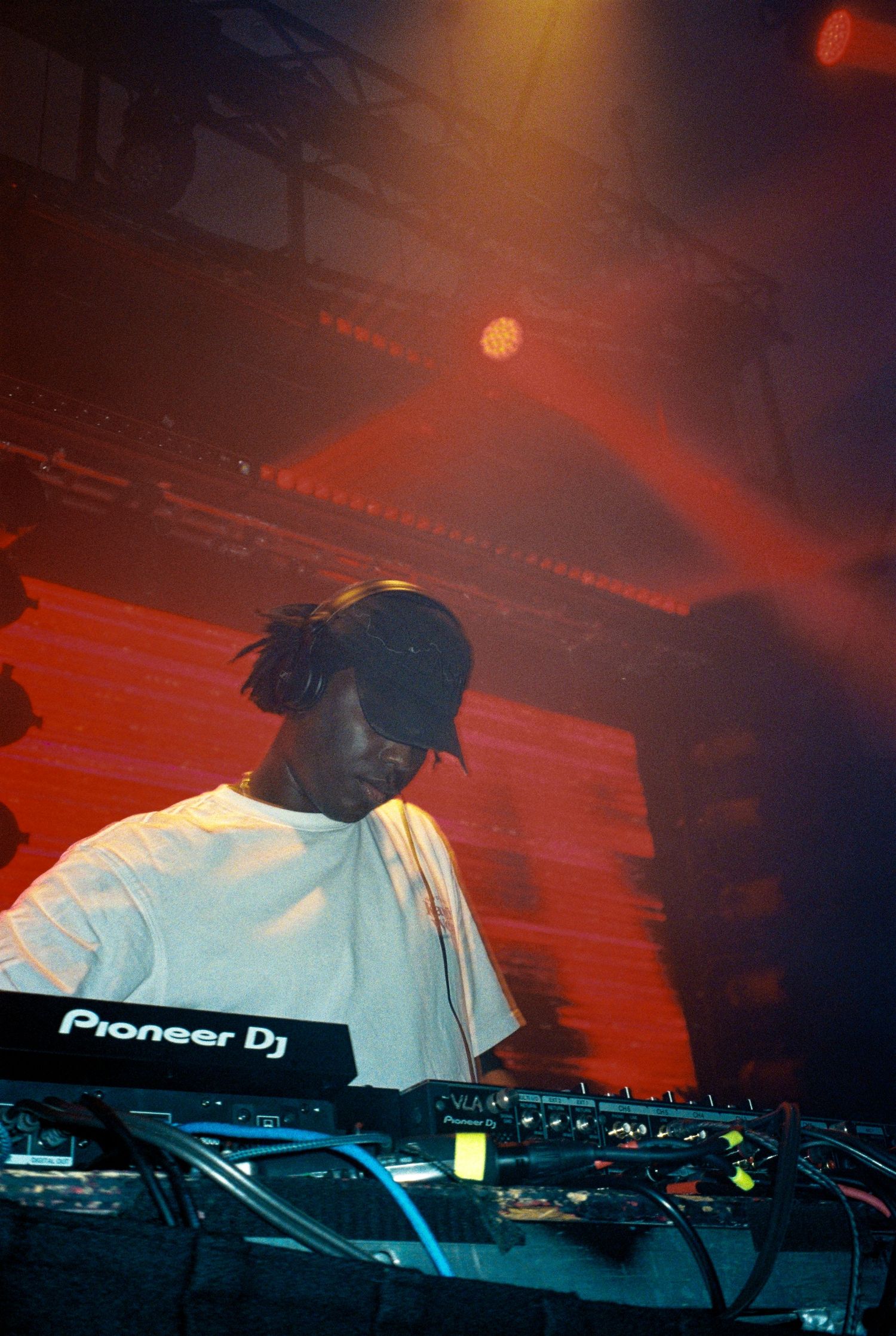 A DJ performs on stage using Pioneer DJ equipment under dramatic red stage lighting in a smoky venue.