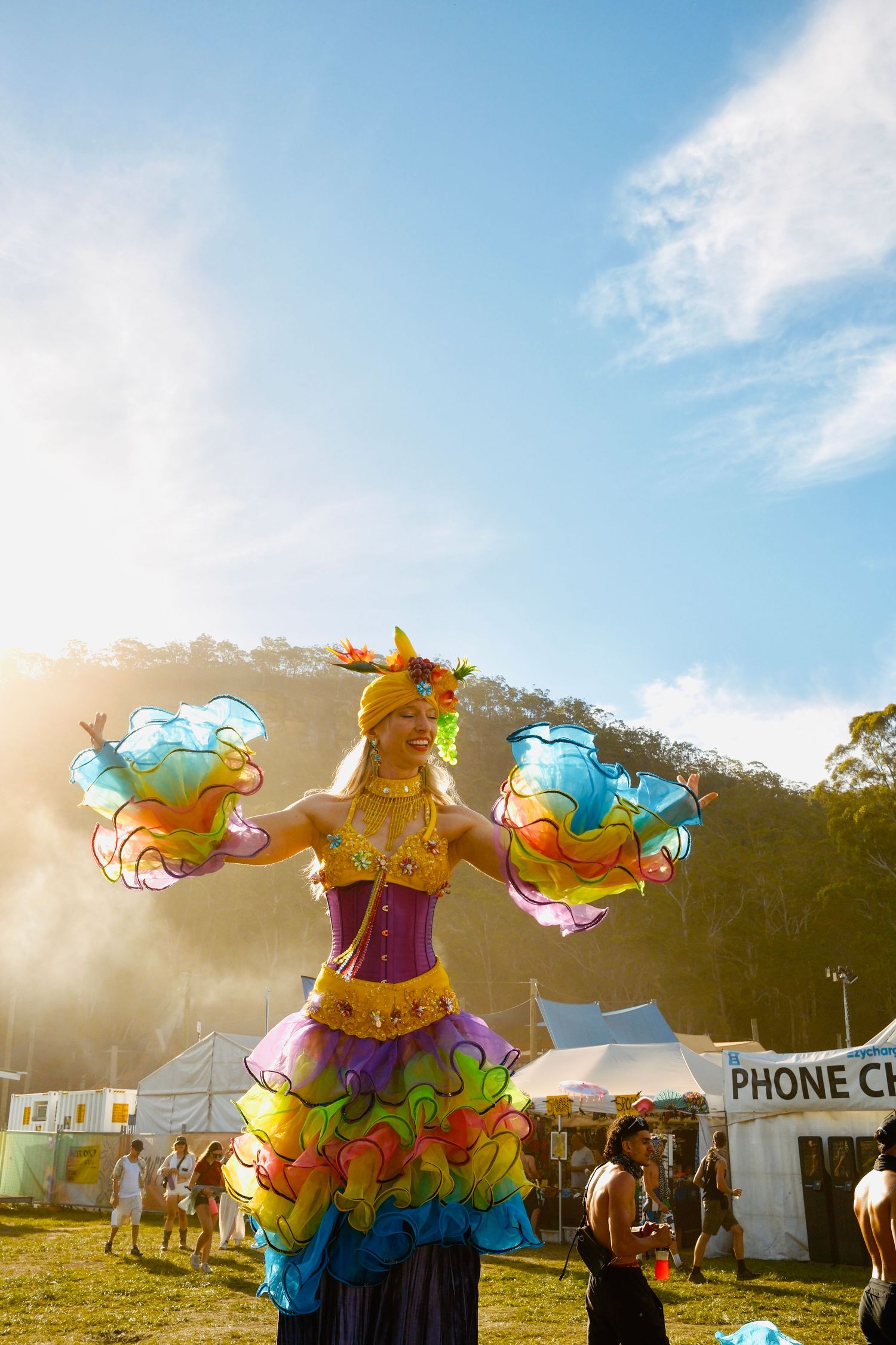 Vibrant stilt walker in rainbow ruffled costume performing at a sunny outdoor festival.