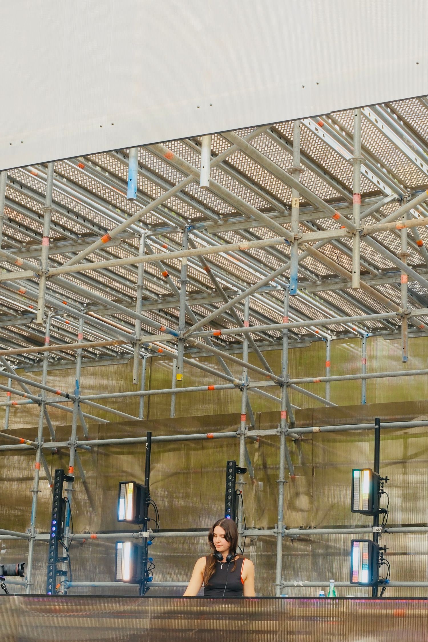 Woman standing behind a reception desk beneath industrial scaffolding and metal framework ceiling in a modern venue.