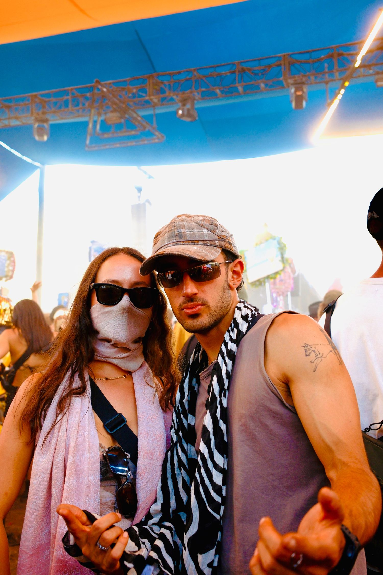 Two festival-goers in sunglasses and patterned scarves posing at a sunny outdoor event.