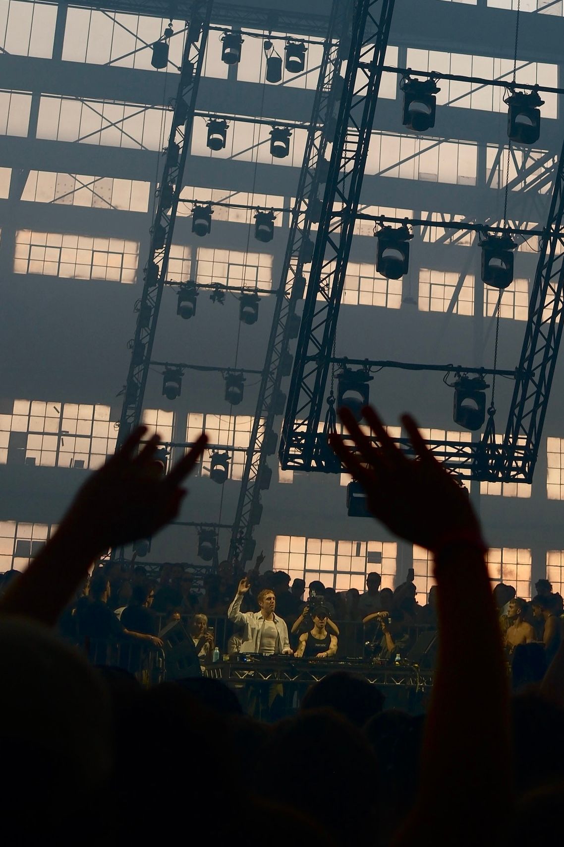 Crowd raises hands toward a performer on stage at a smoky indoor warehouse music event.