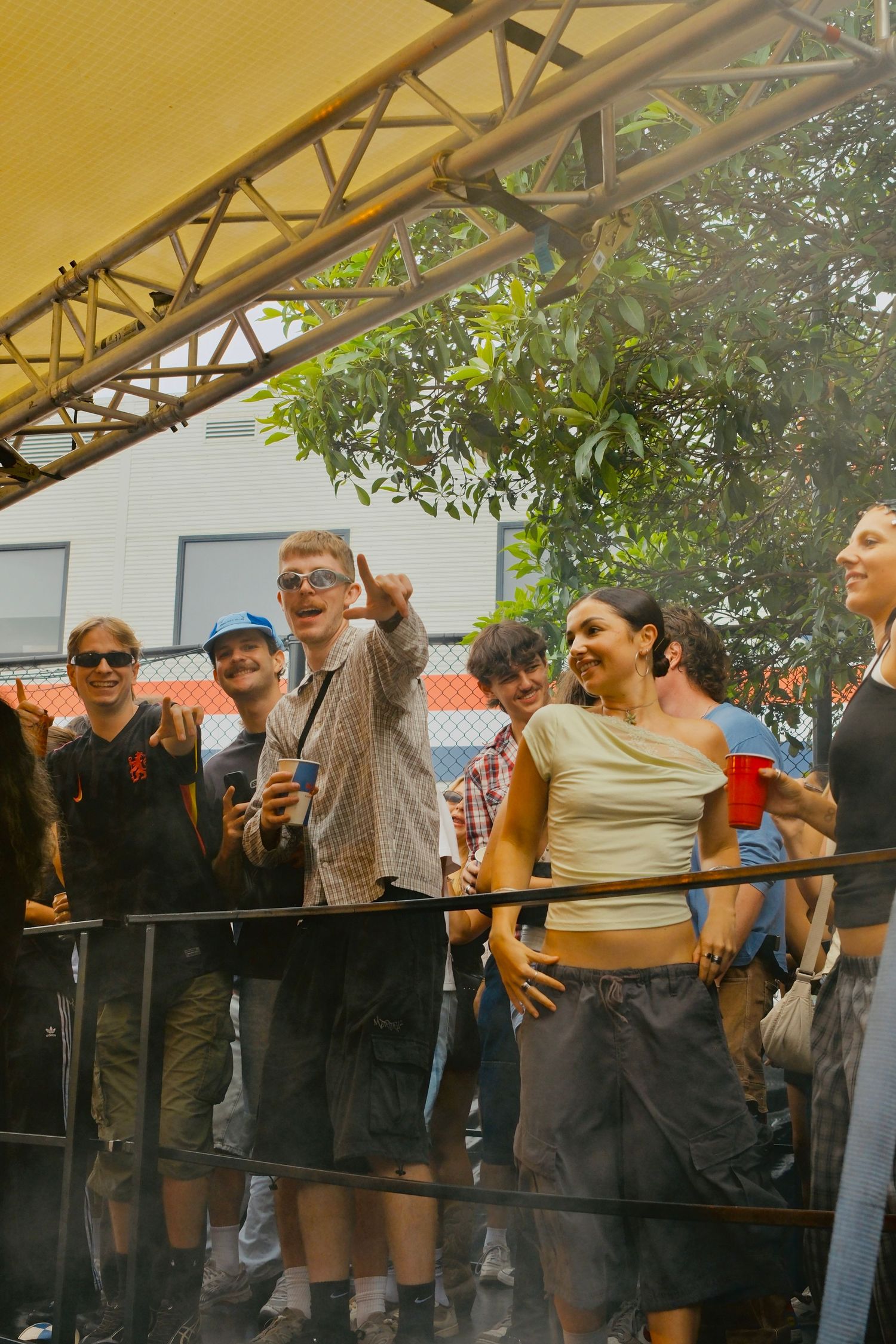 Group of young people cheering and dancing near a railing at an outdoor music festival.