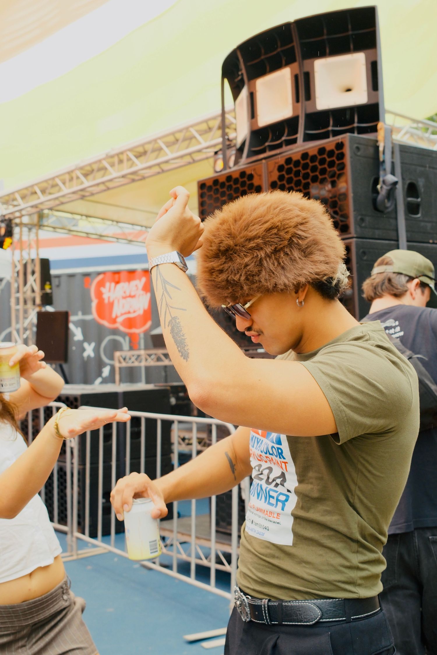 Young person with curly hair and tattoos dancing energetically at an outdoor music festival.