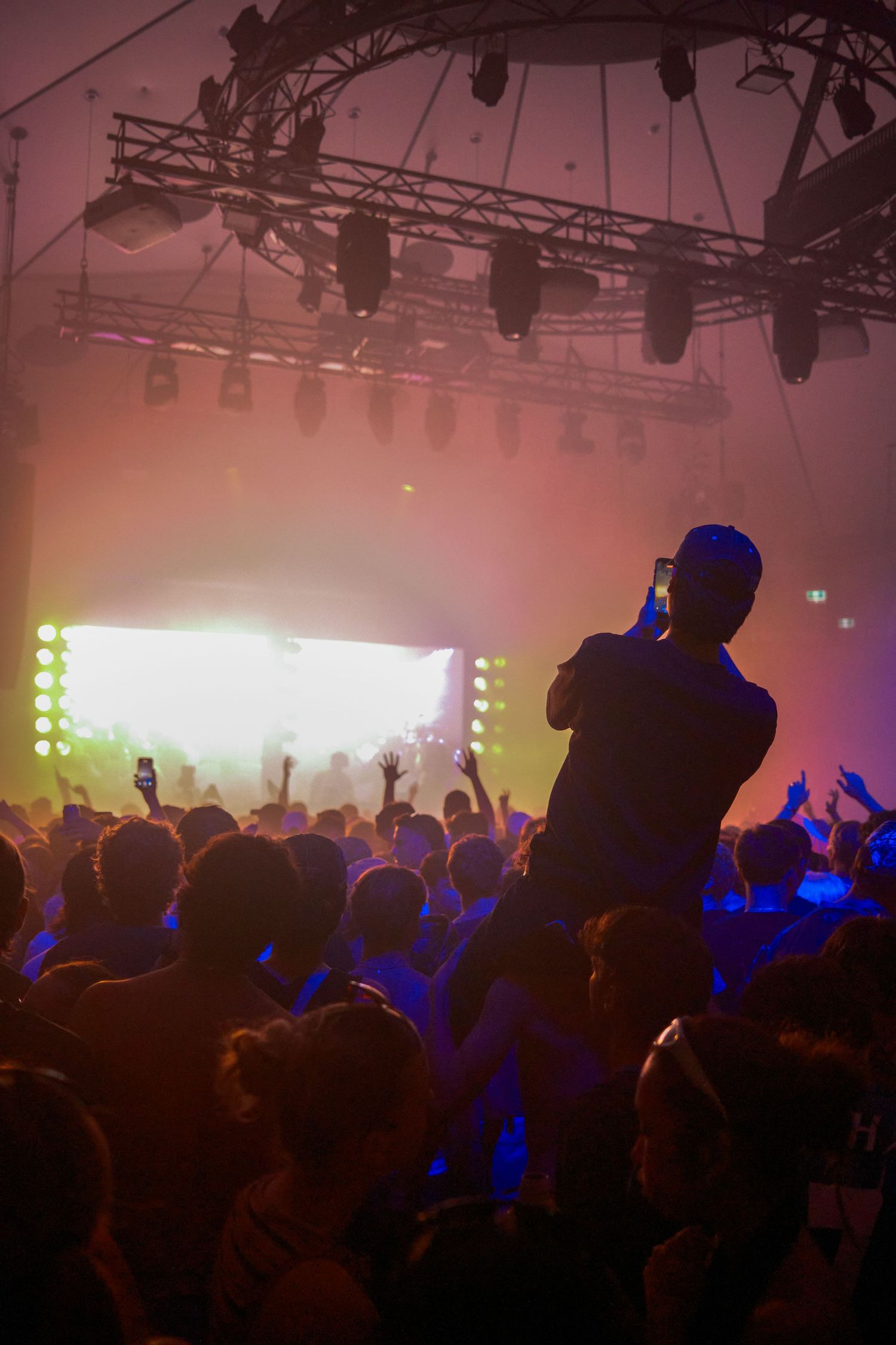 Crowd of concert-goers silhouetted against bright stage lights at an indoor music festival.