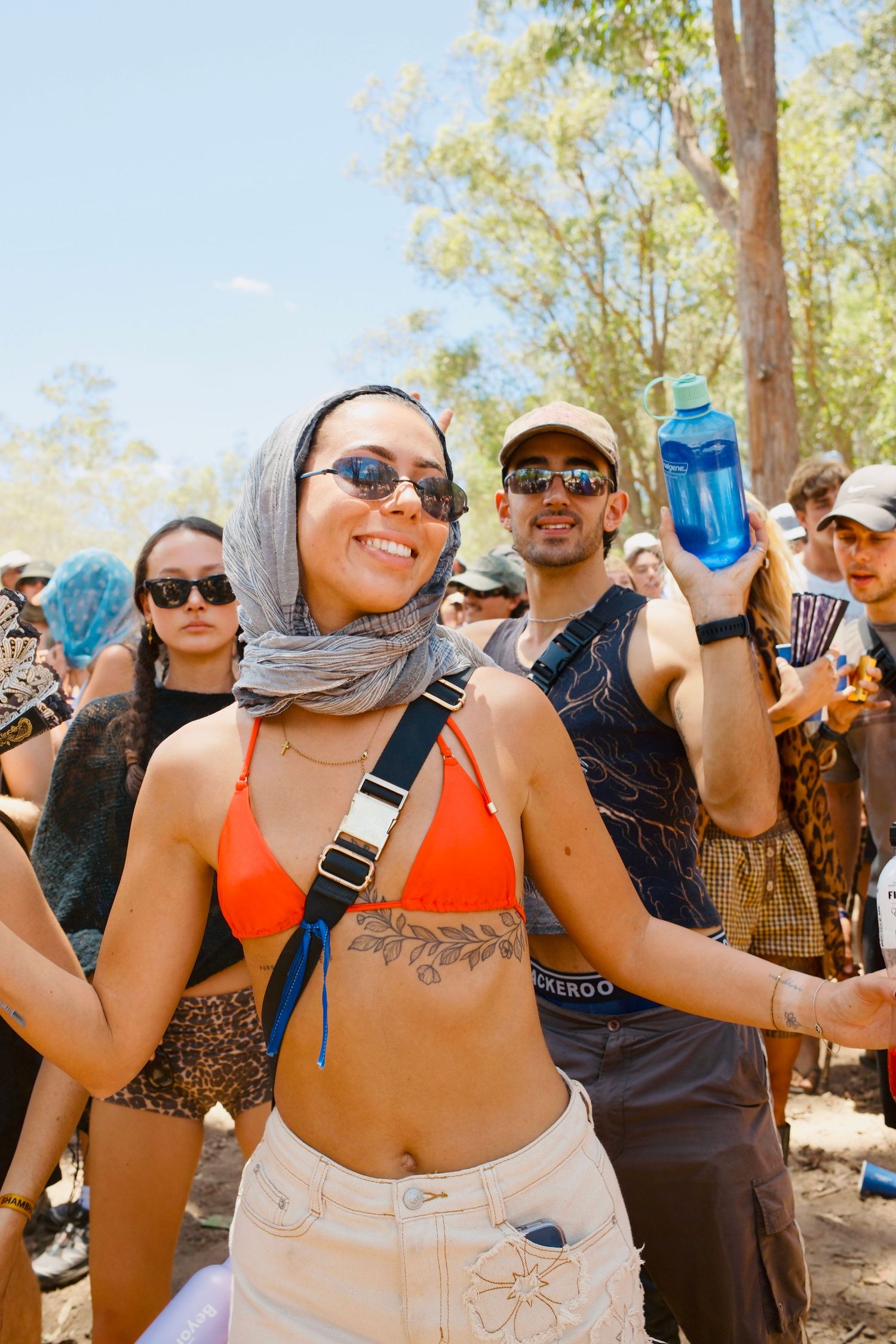 Smiling woman in orange bikini top and headscarf dancing at an outdoor music festival.