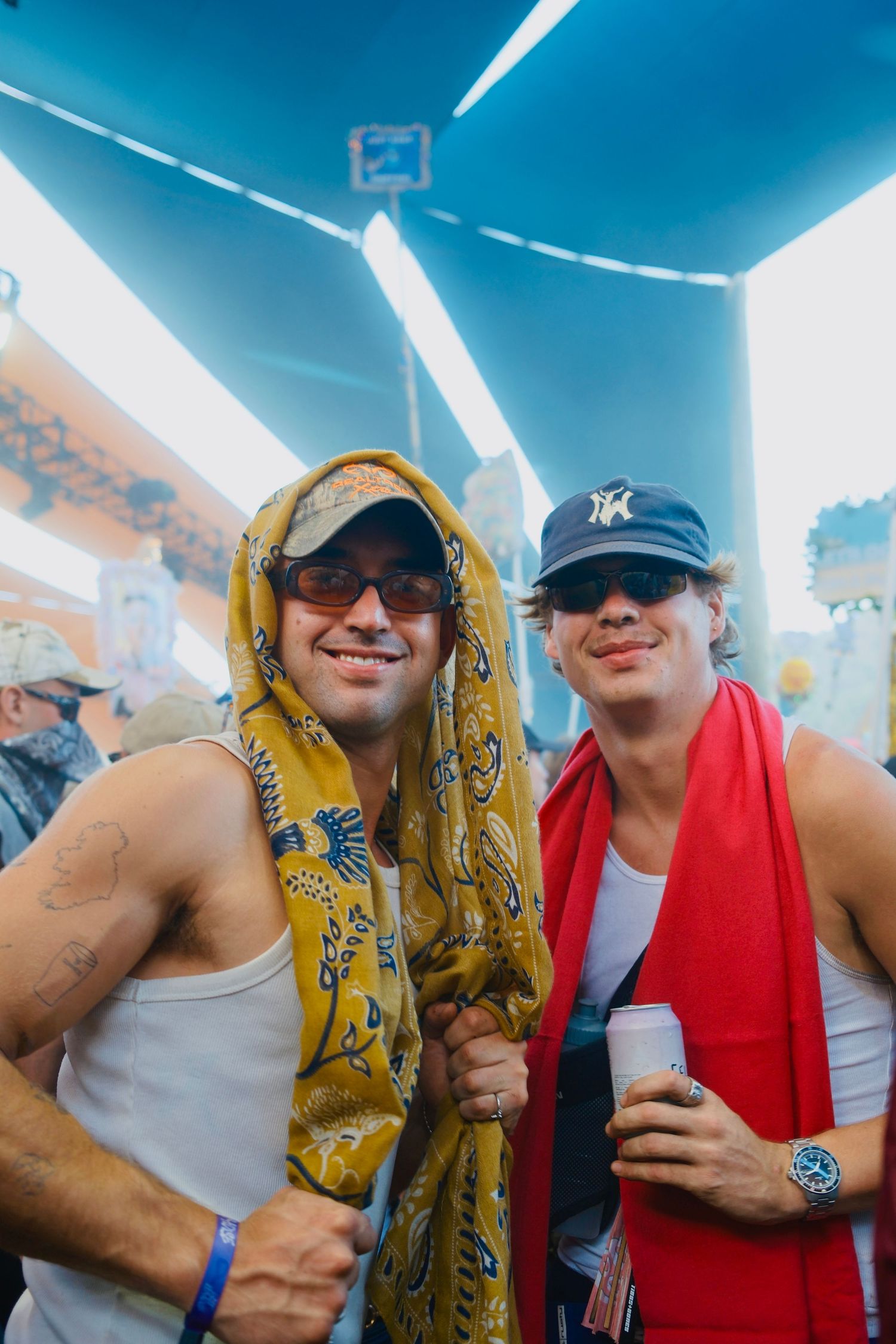 Two smiling men with scarves and caps posing together at a music festival.
