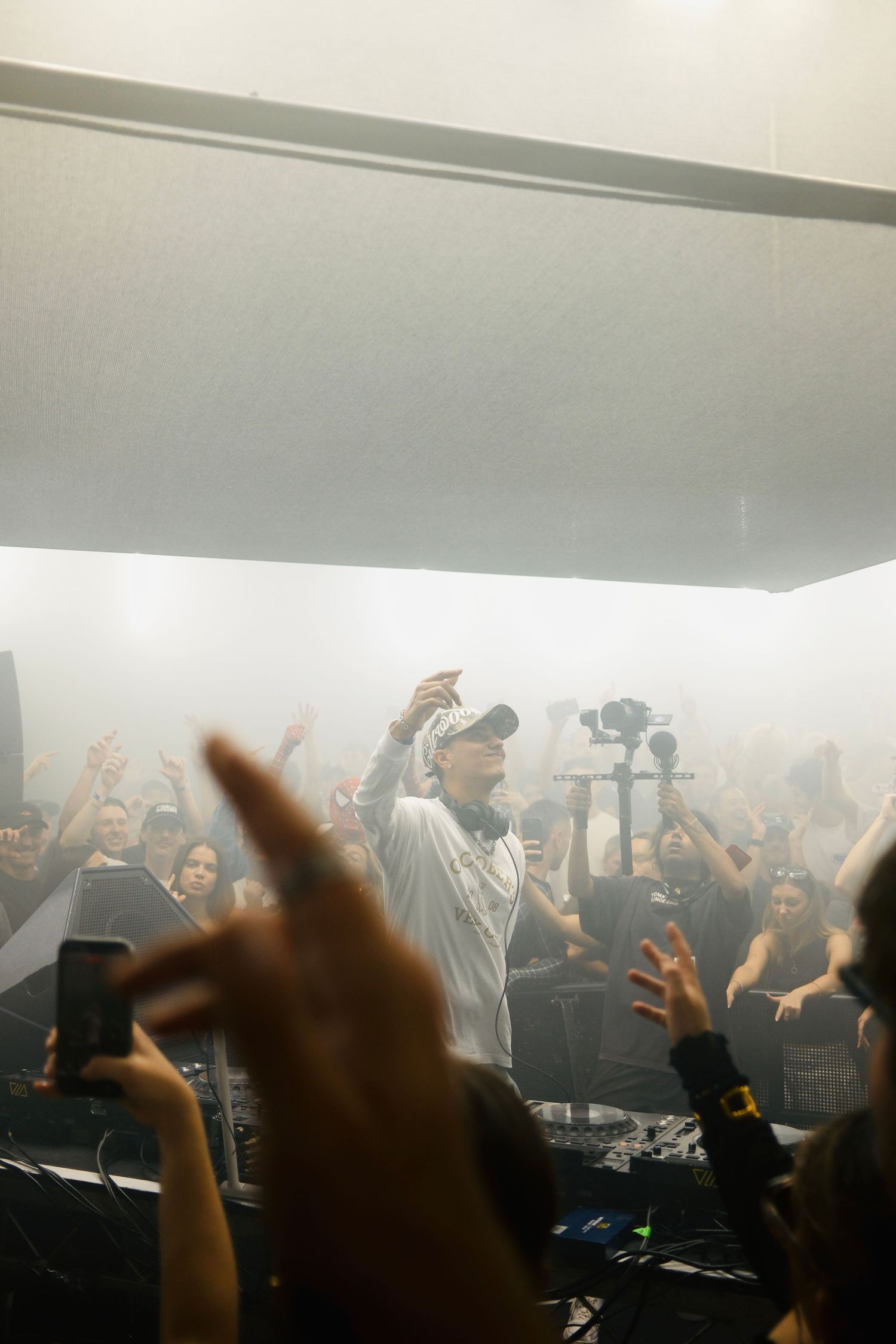 DJ in white cap performing amid heavy fog for an energetic crowd at an indoor nightclub event.