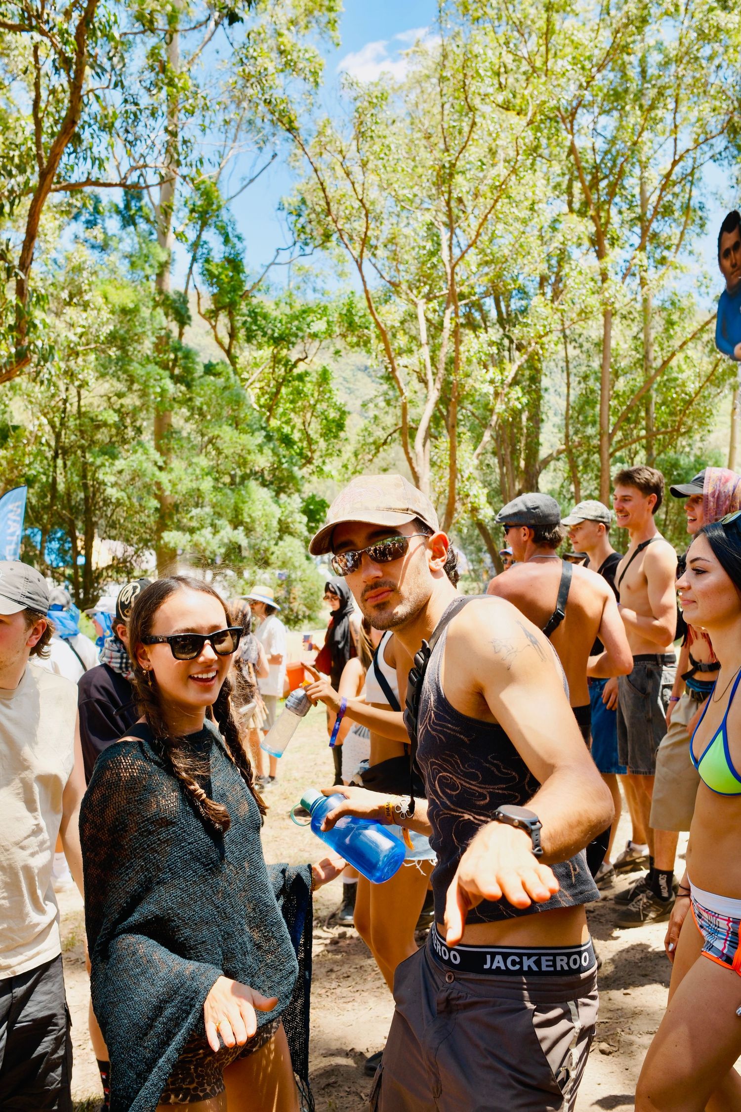 Couple smiling and dancing together at a sunny outdoor music festival in the woods.