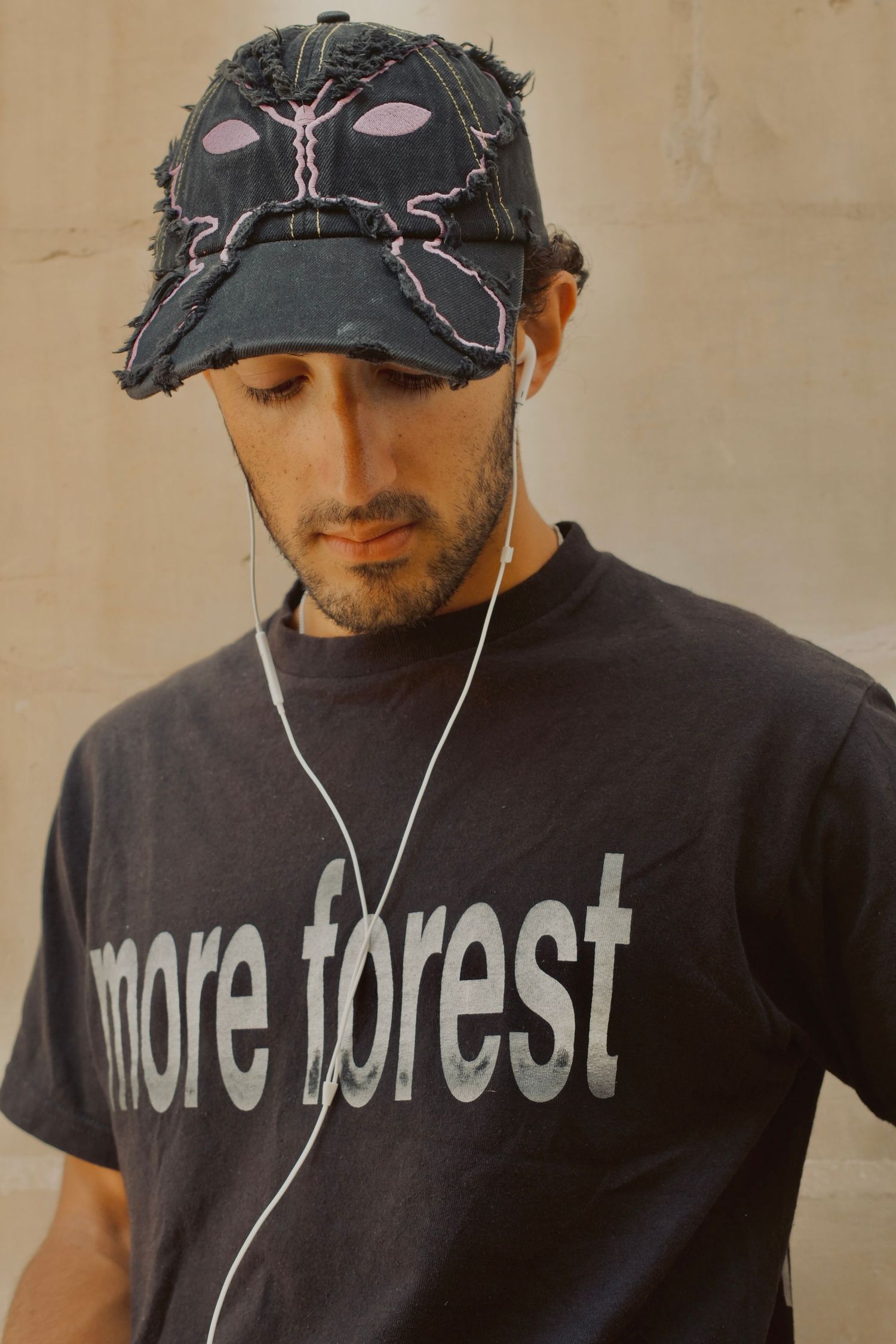 Young man wearing a distressed cap and black more forest t-shirt listening to music with earphones.