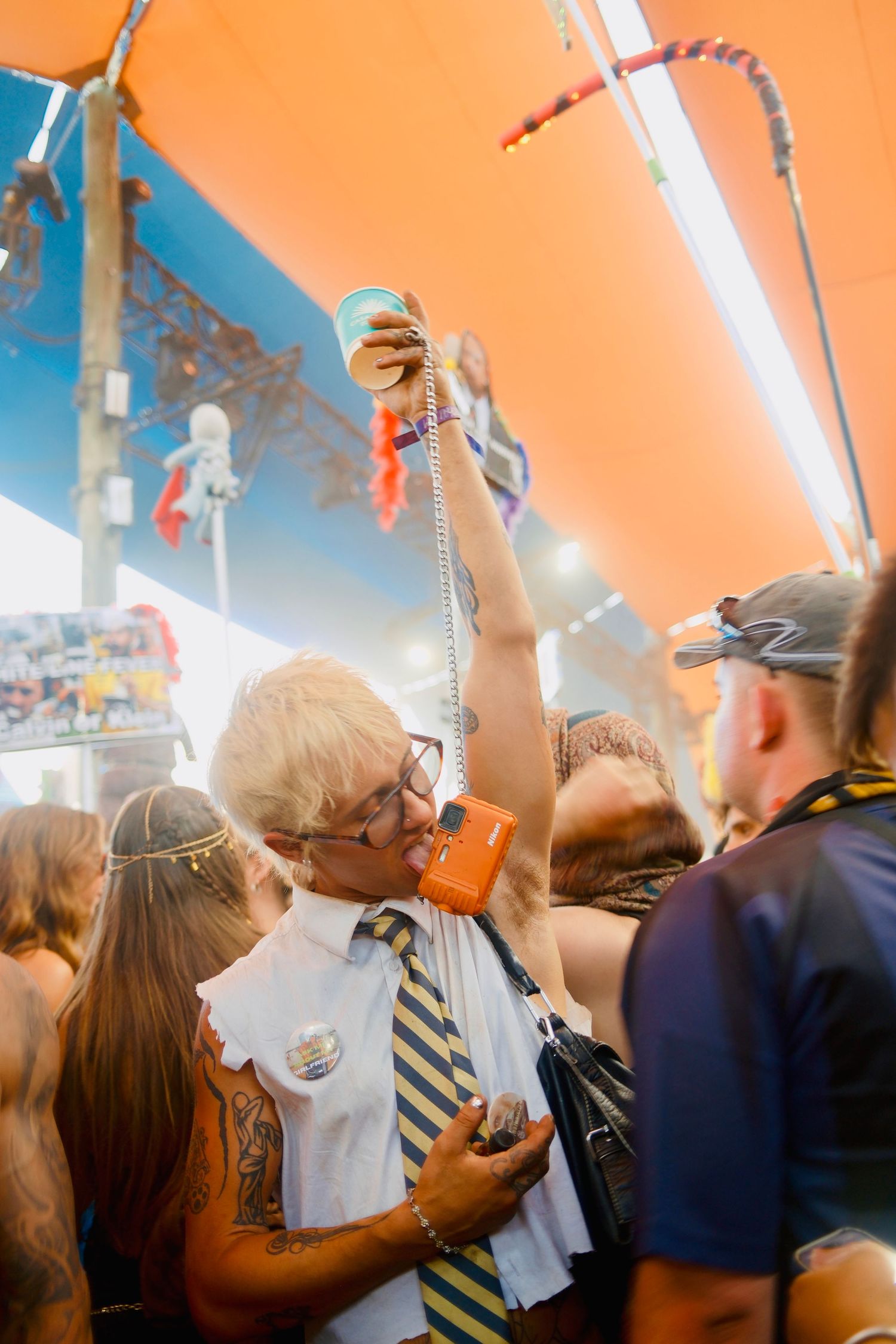Elderly man in costume holding drinks aloft in a crowded colorful festival tent.