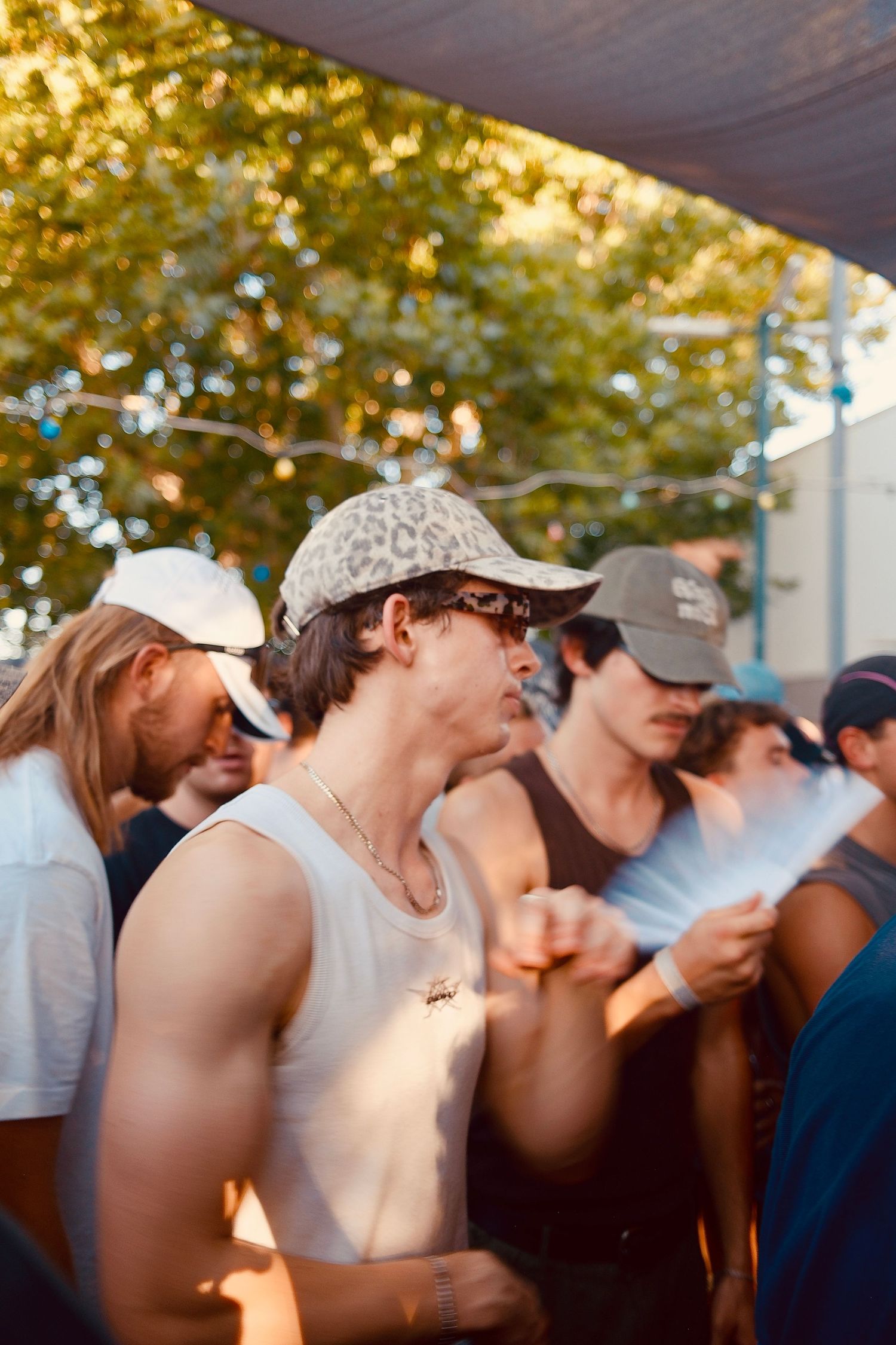 Young man in a leopard print cap dances in a crowd at a sunny outdoor festival.