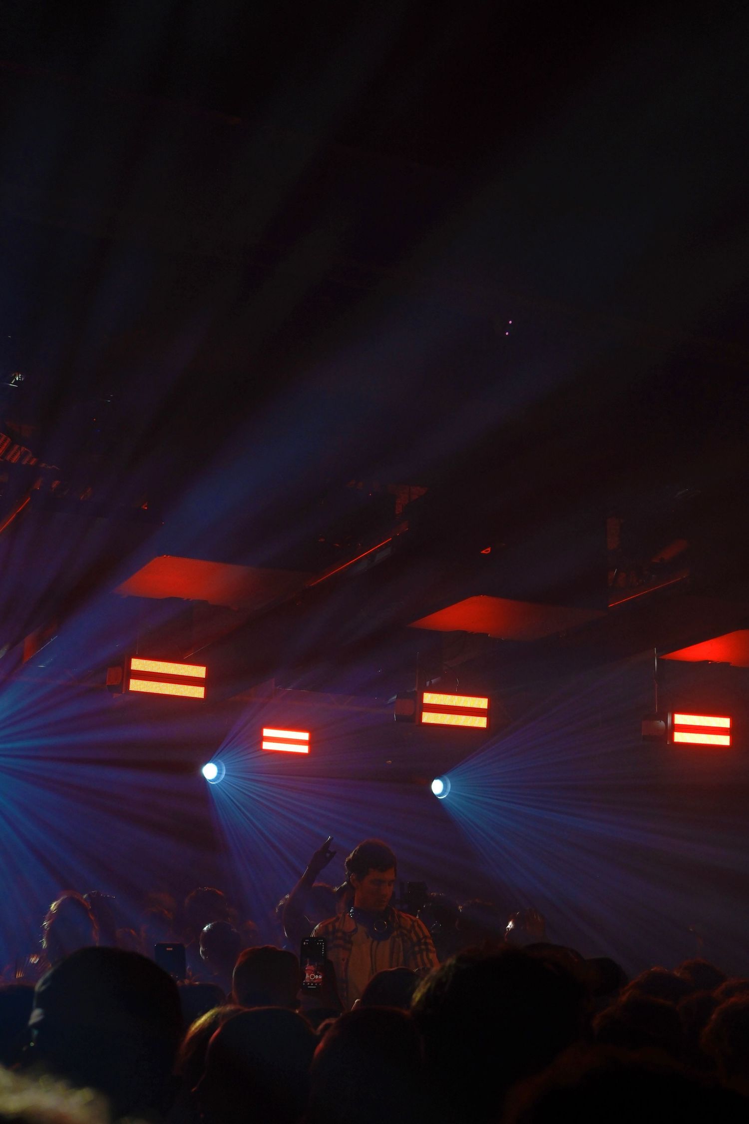 Performer on stage with crowd as red and blue laser lights beam through a dark concert venue.