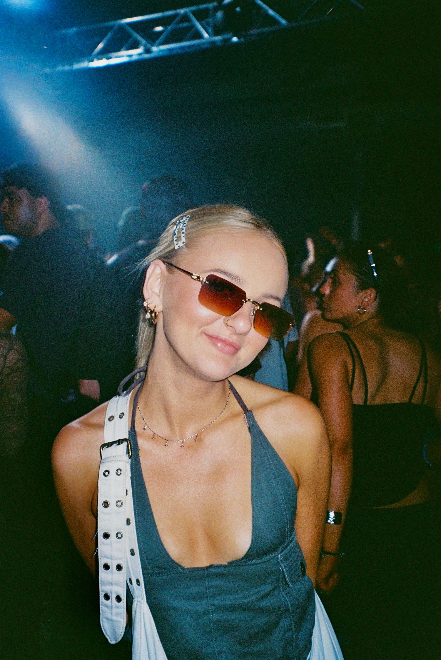 Blonde woman in sunglasses and denim halter top posing at nightclub party.