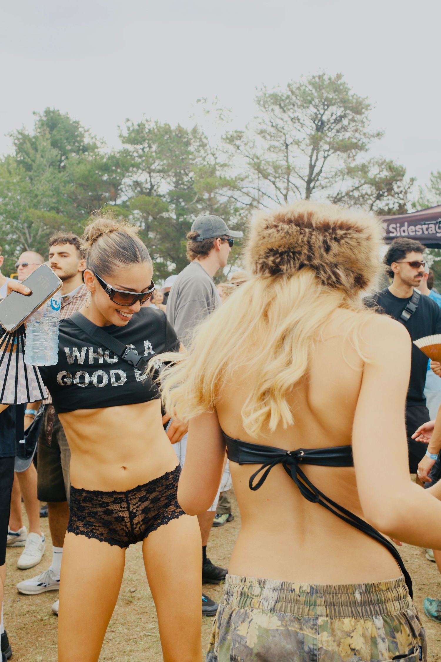 Festival attendees dancing outdoors with a woman wearing a black crop top and lace shorts at a summer music event.