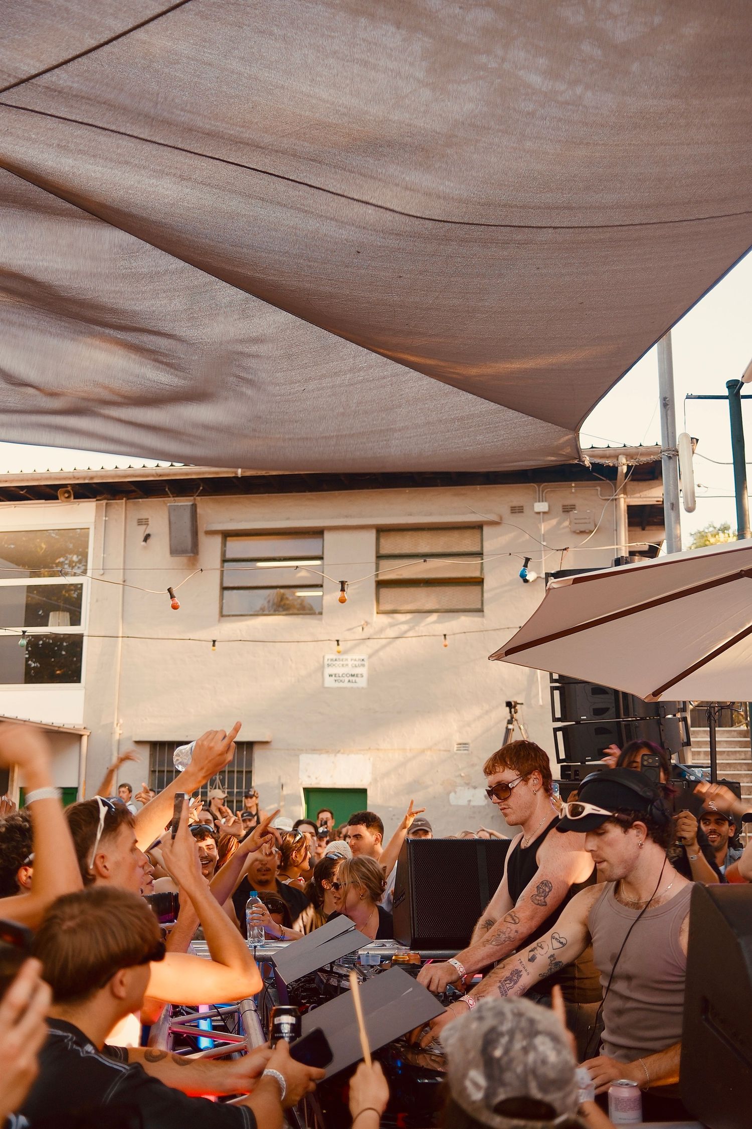 Tattooed DJ performs for an energetic crowd at a sunny outdoor daytime music event.