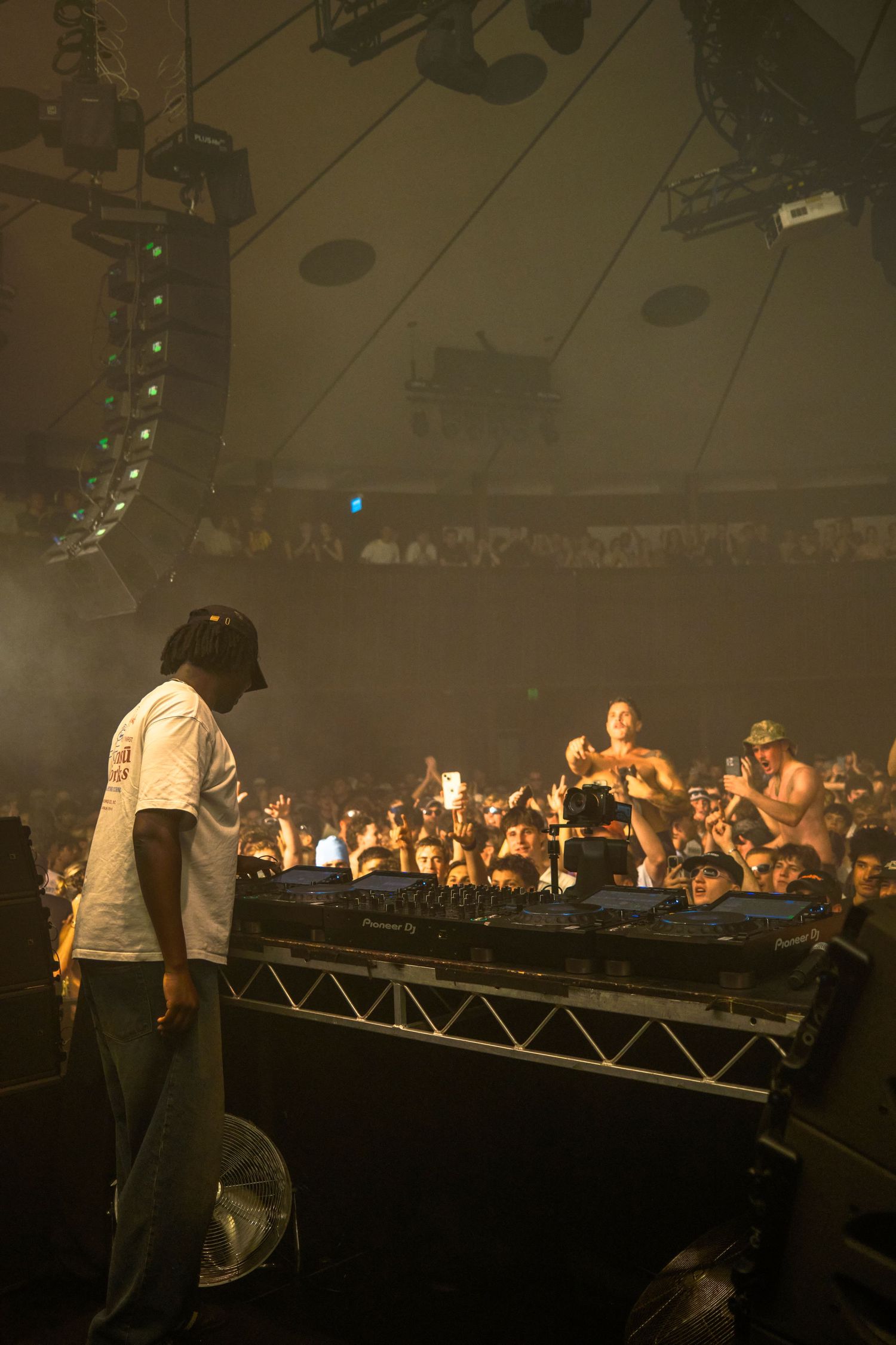 DJ performing on stage at a packed music festival, with crowd and dramatic lighting in a large tent venue.